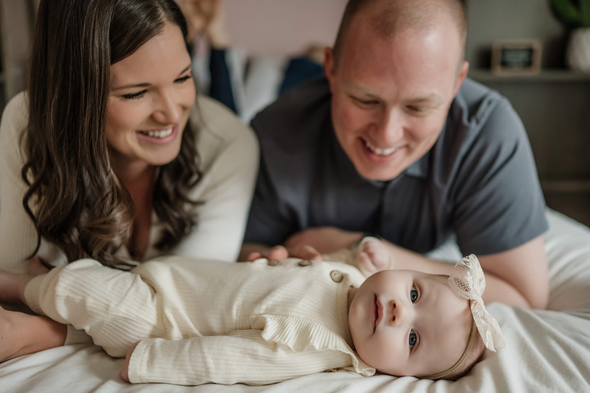 Mom and dad lying on their bed with their baby girl in front of them, all smiling