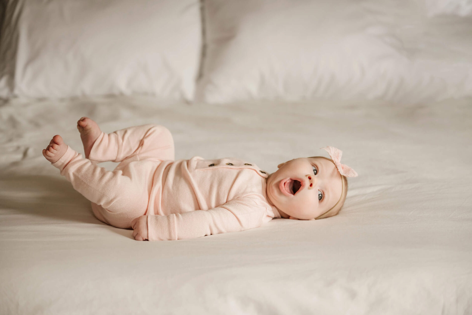 A cute newborn girl smiling and lying on her parent's bed with her mouth wide open