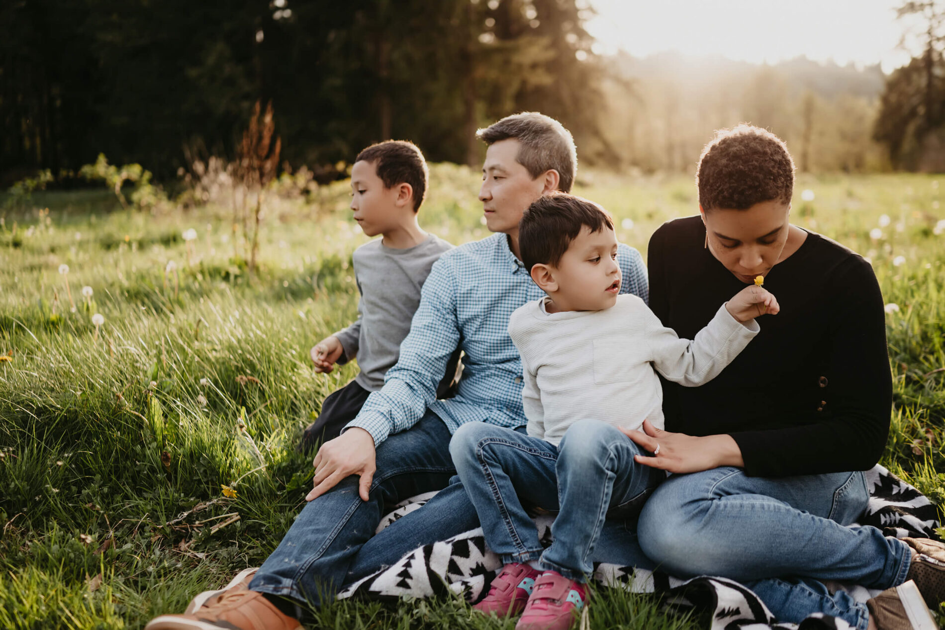 A man gazing forward sitting in a field with his wife and two sons during sunset