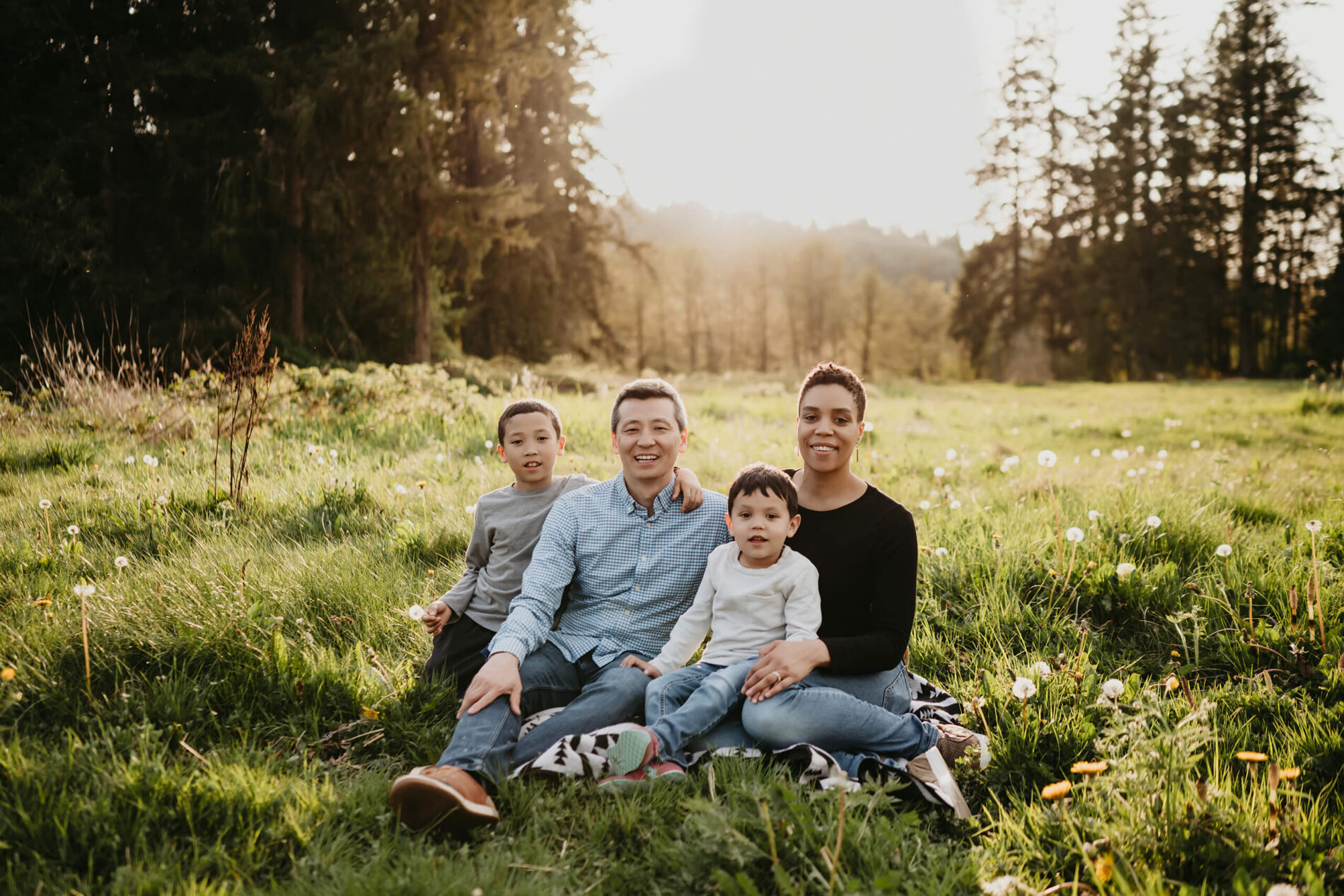 Mom, dad, and two sons sitting in a meadow in a beautiful park in Redmond, WA during sunset