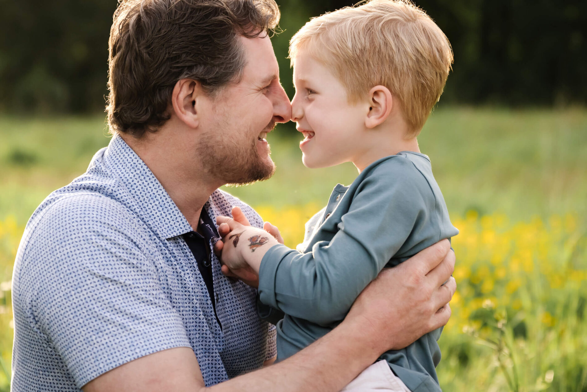 Father and child touching noses and laughing during a close-up outdoor family portrait.