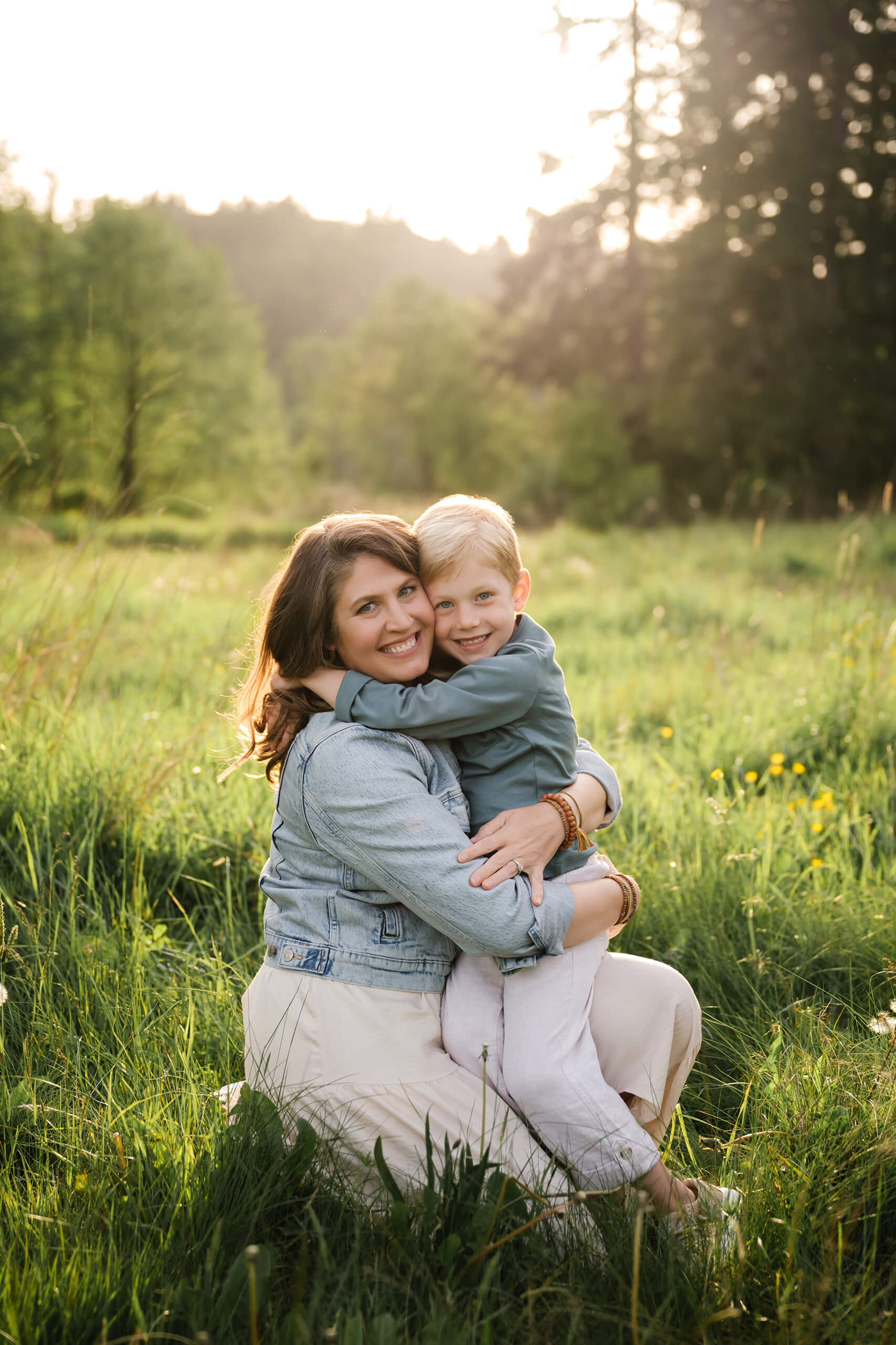 Mother hugging her child in a sunny meadow with soft green trees in the background.