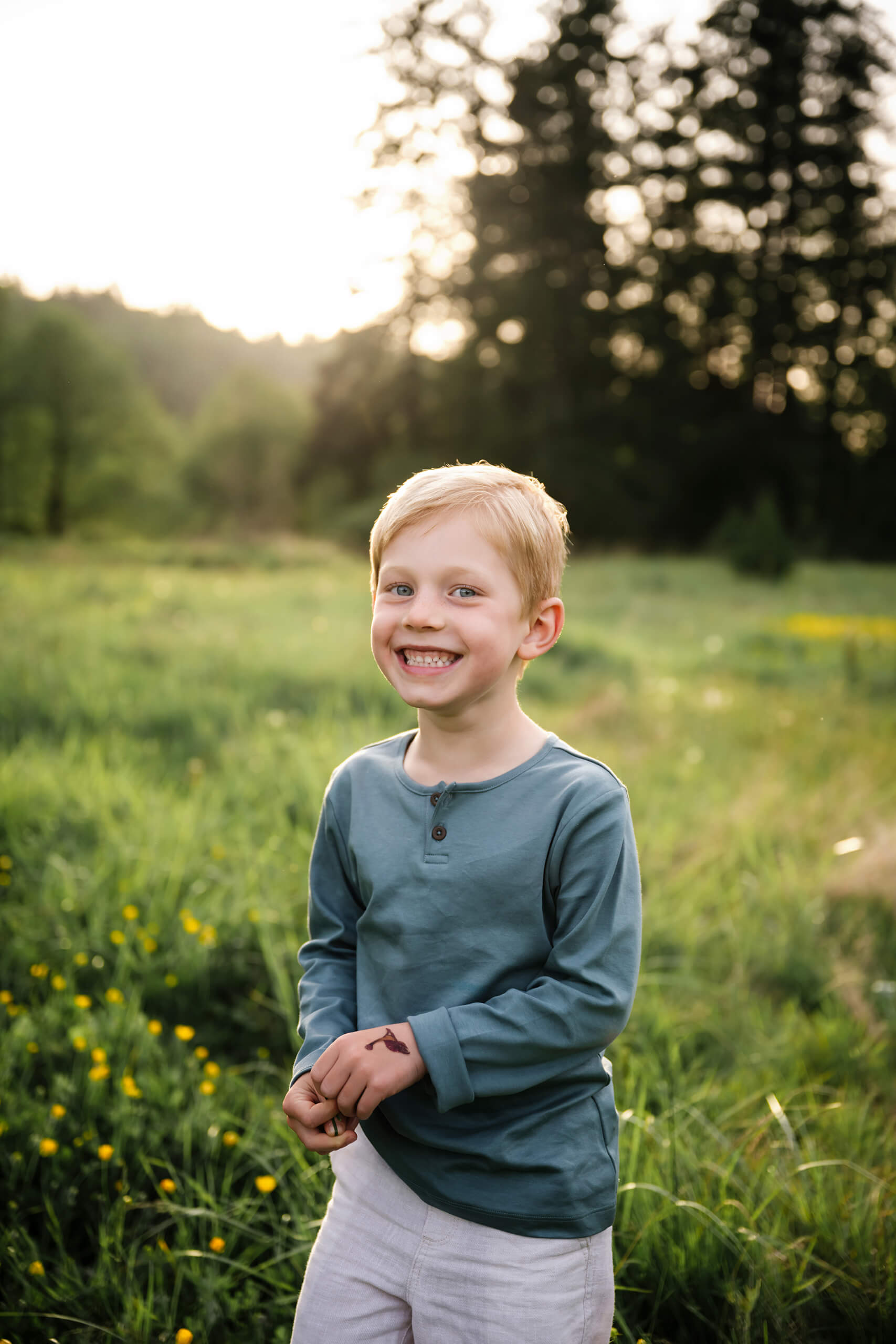 Smiling child standing in a grassy field with small yellow flowers during an outdoor family photo session.