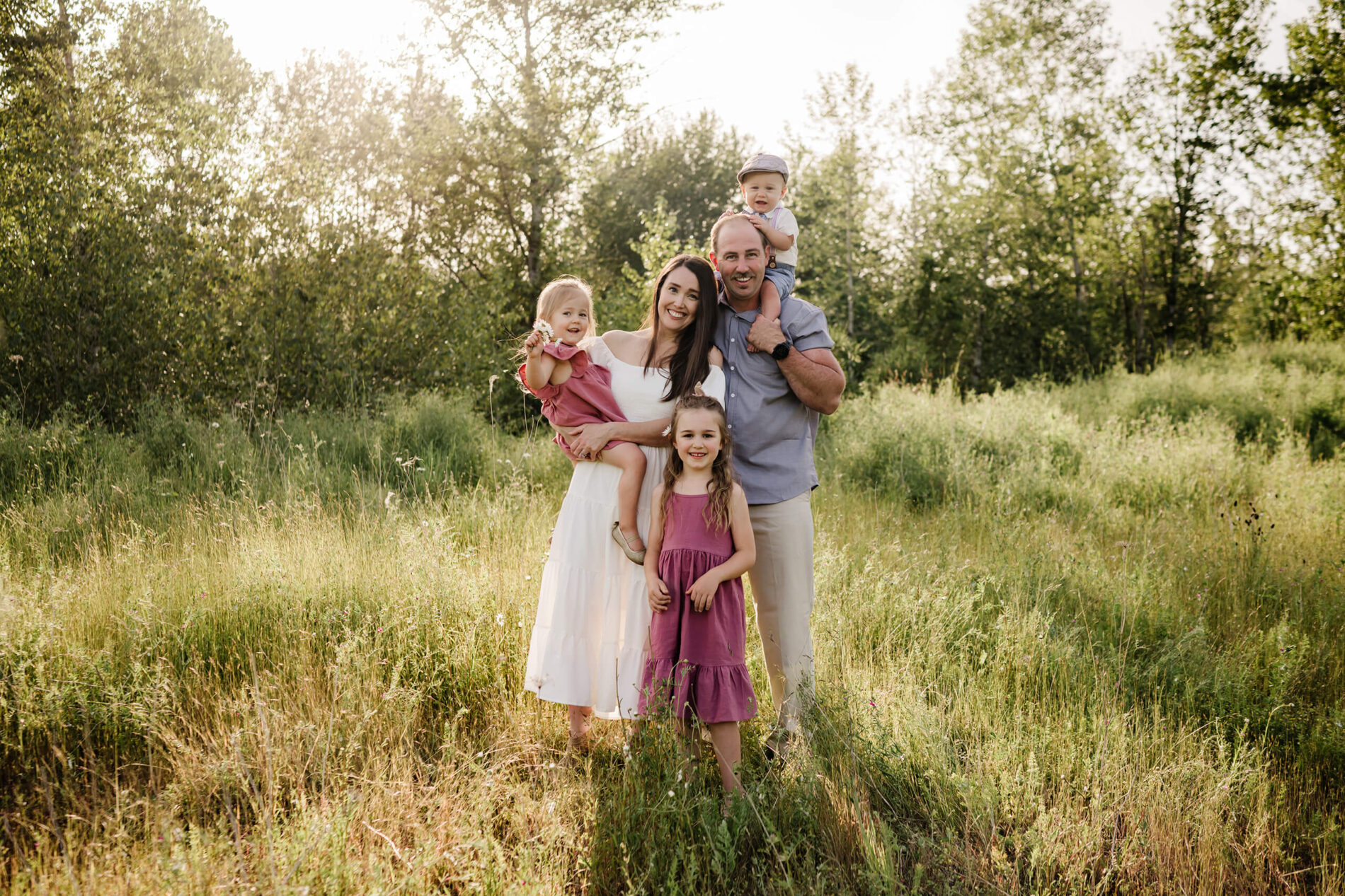 Family of five standing together in a tall grassy field during a sunny outdoor family session.