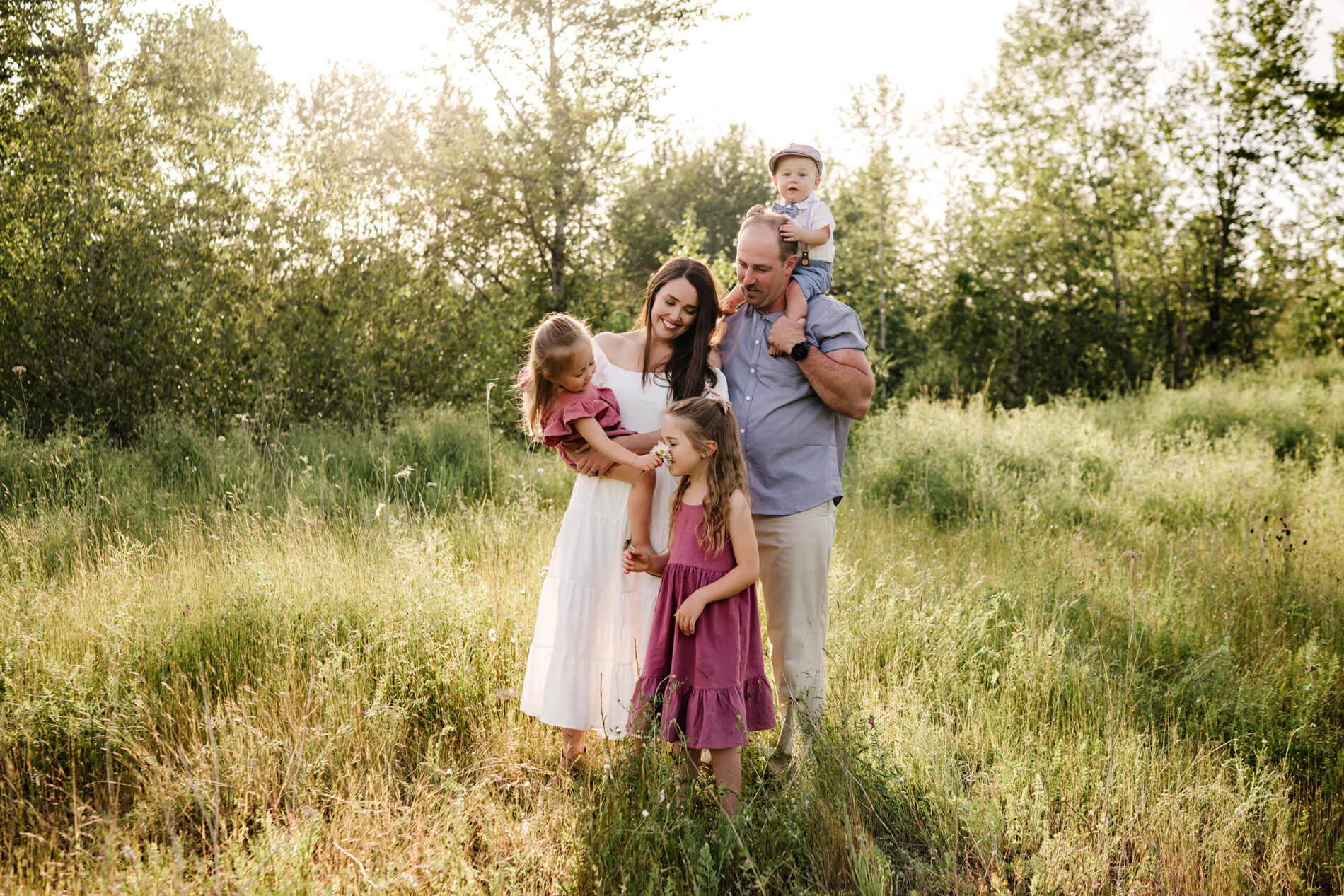 Parents and three children standing together in a meadow while one child holds a small flower.