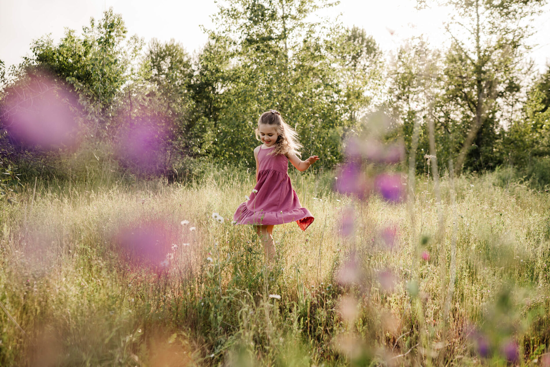 Young girl twirling in a sunlit meadow during an outdoor family photo session.
