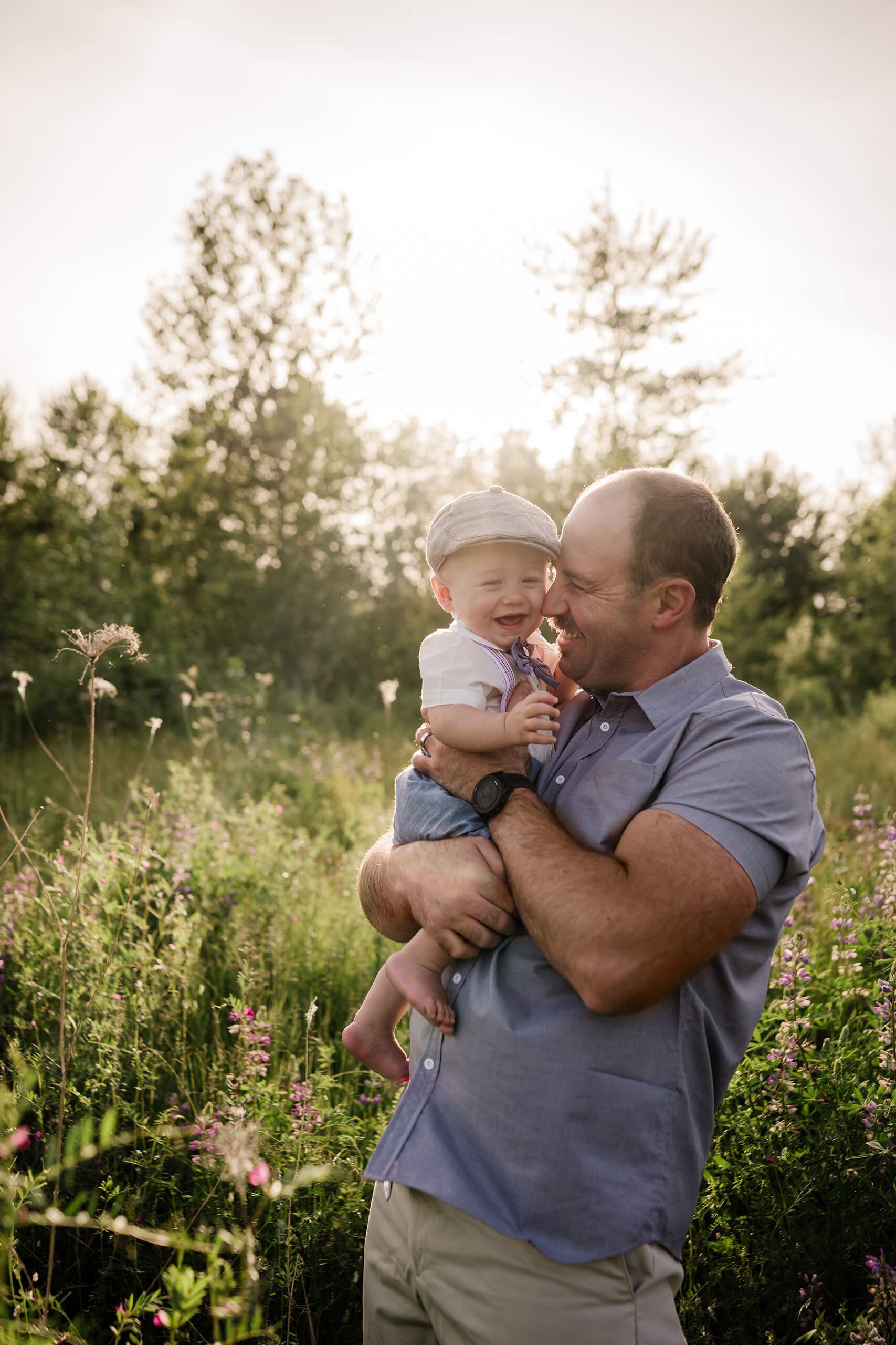 Father holding his laughing baby in a wildflower meadow during golden hour.