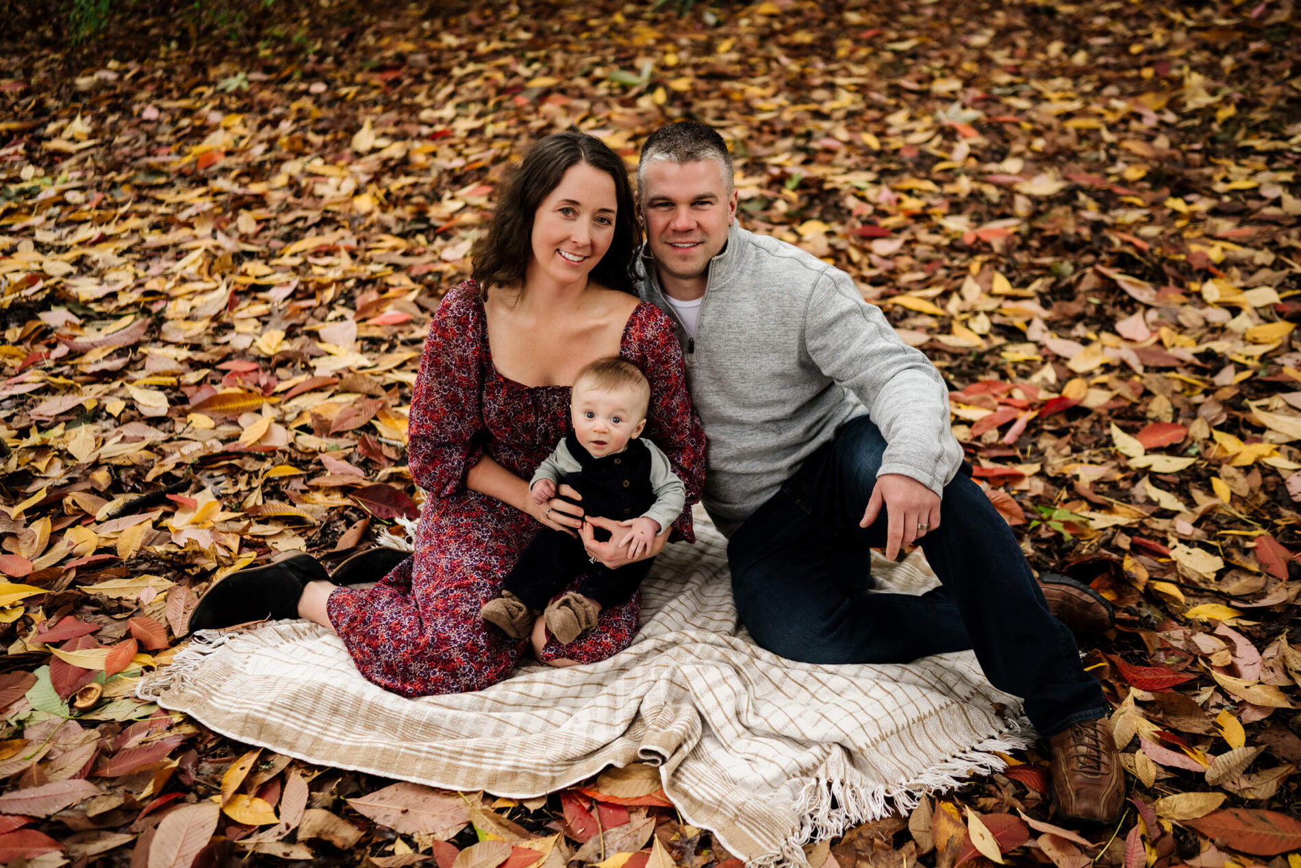 Mom and dad sitting on a blanket with their cute son with fall leaves in the background