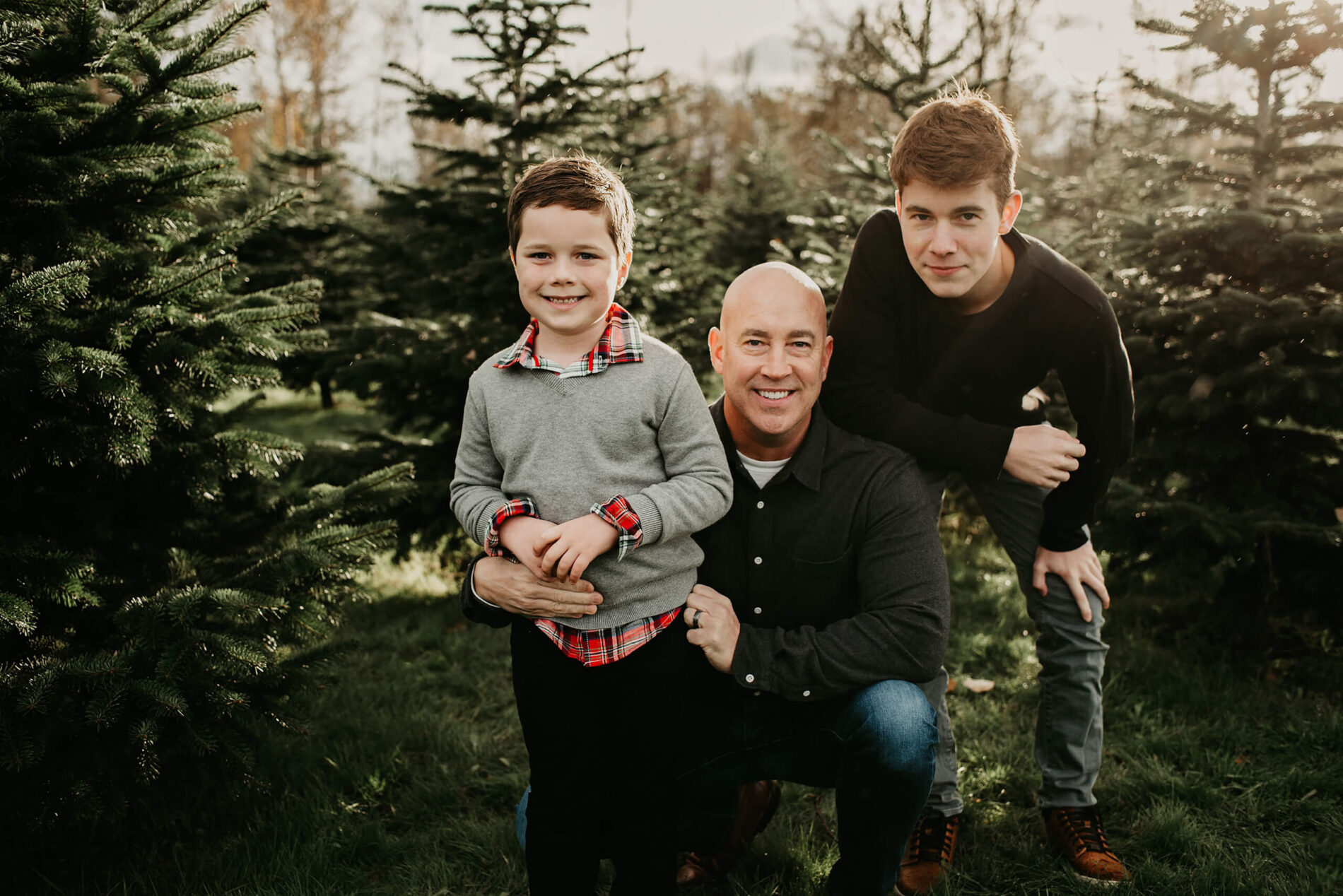 Dad posing with two sons at a Christmas tree farm