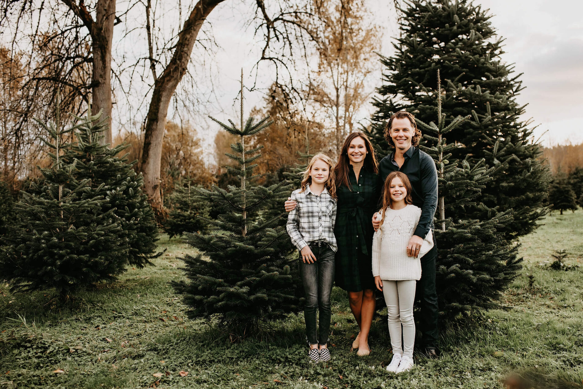 Mom, dad, and two daughters posing at a Christmas tree farm