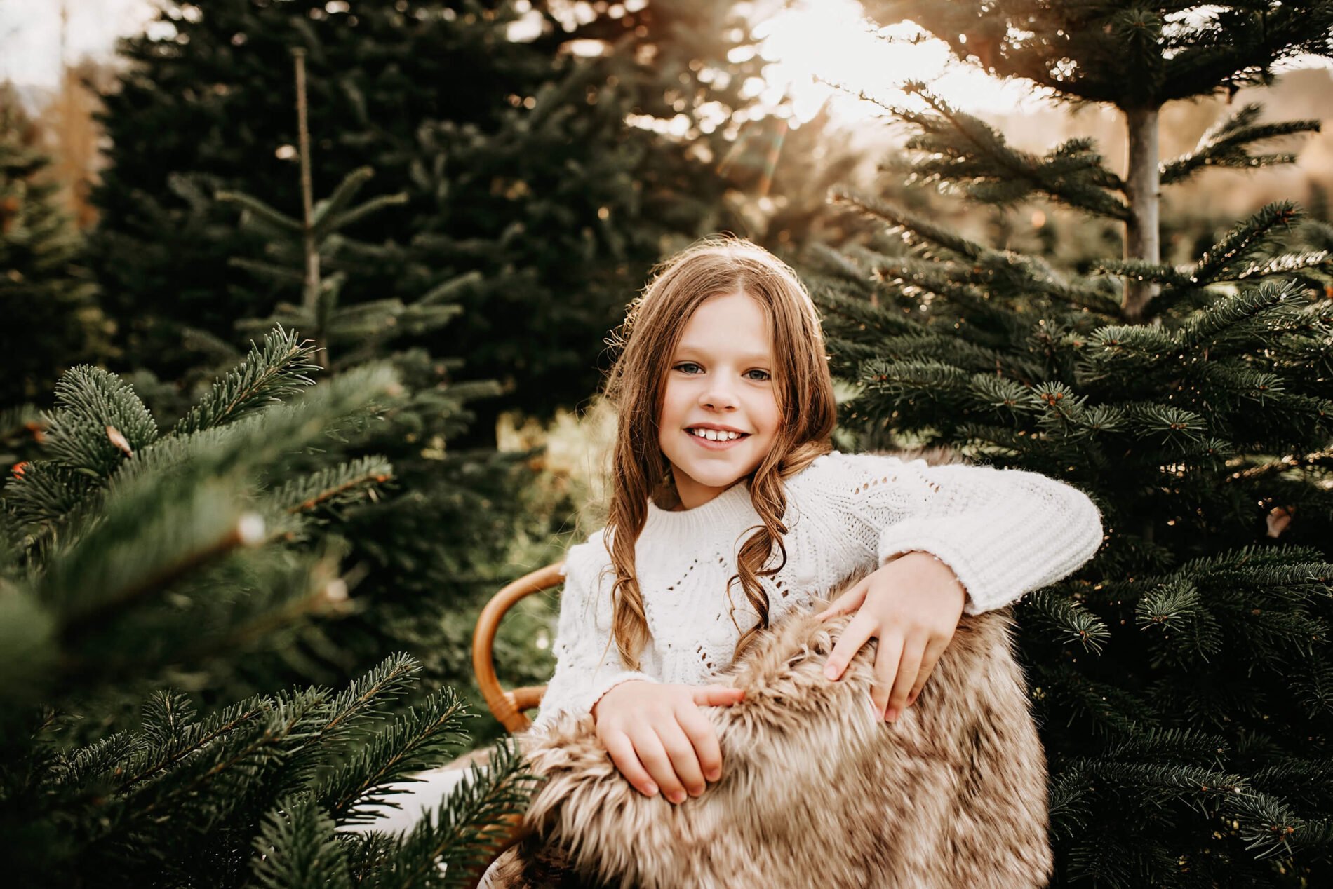 A young girl sitting in a cozy wooden chair at a Christmas tree farm