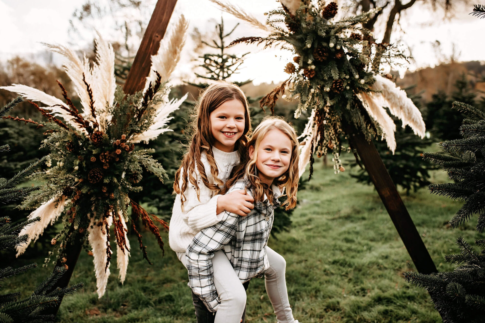 A teenage girl giving a piggy back ride to her younger sister at a Christmas tree farm