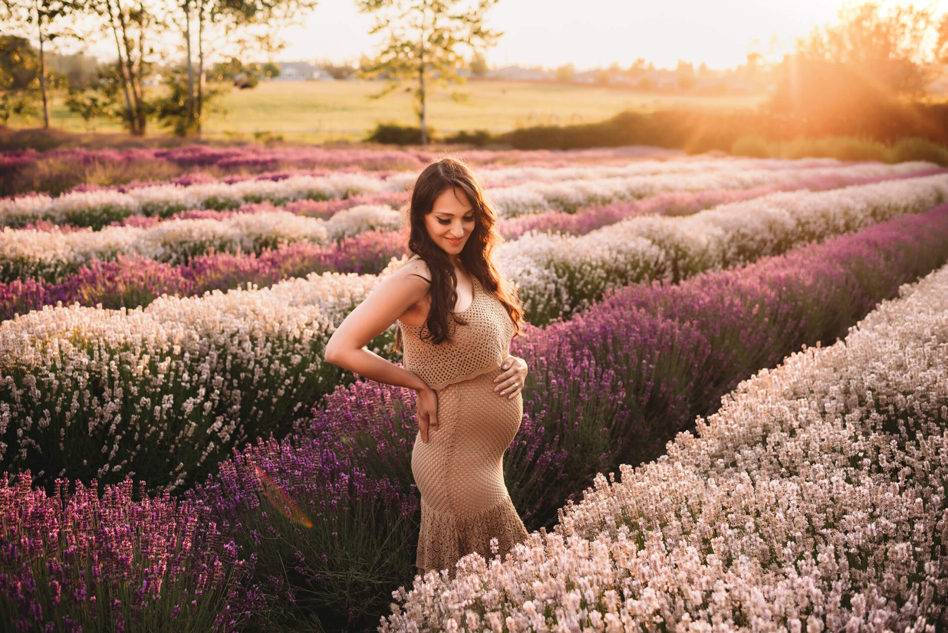 Smiling pregnant woman in a dress standing in a beautiful lavender field during sunset