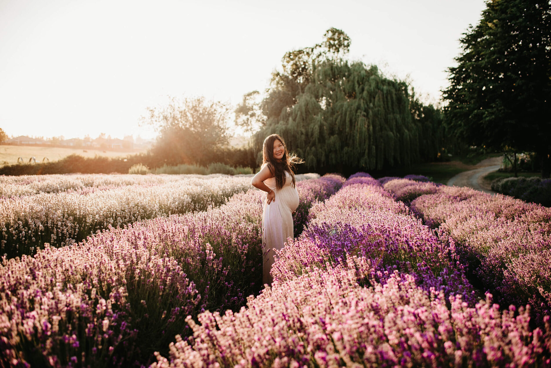 A smiling young pregnant woman in a maternity gown posing in a lavender field