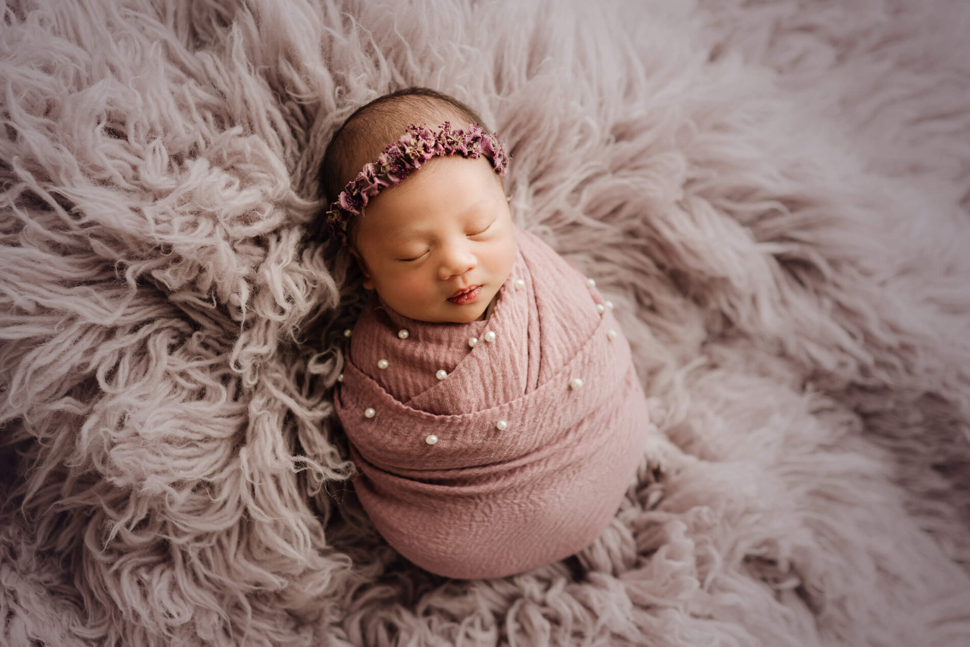 A beautiful newborn girl wrapped in lavender colored blanket sleeping