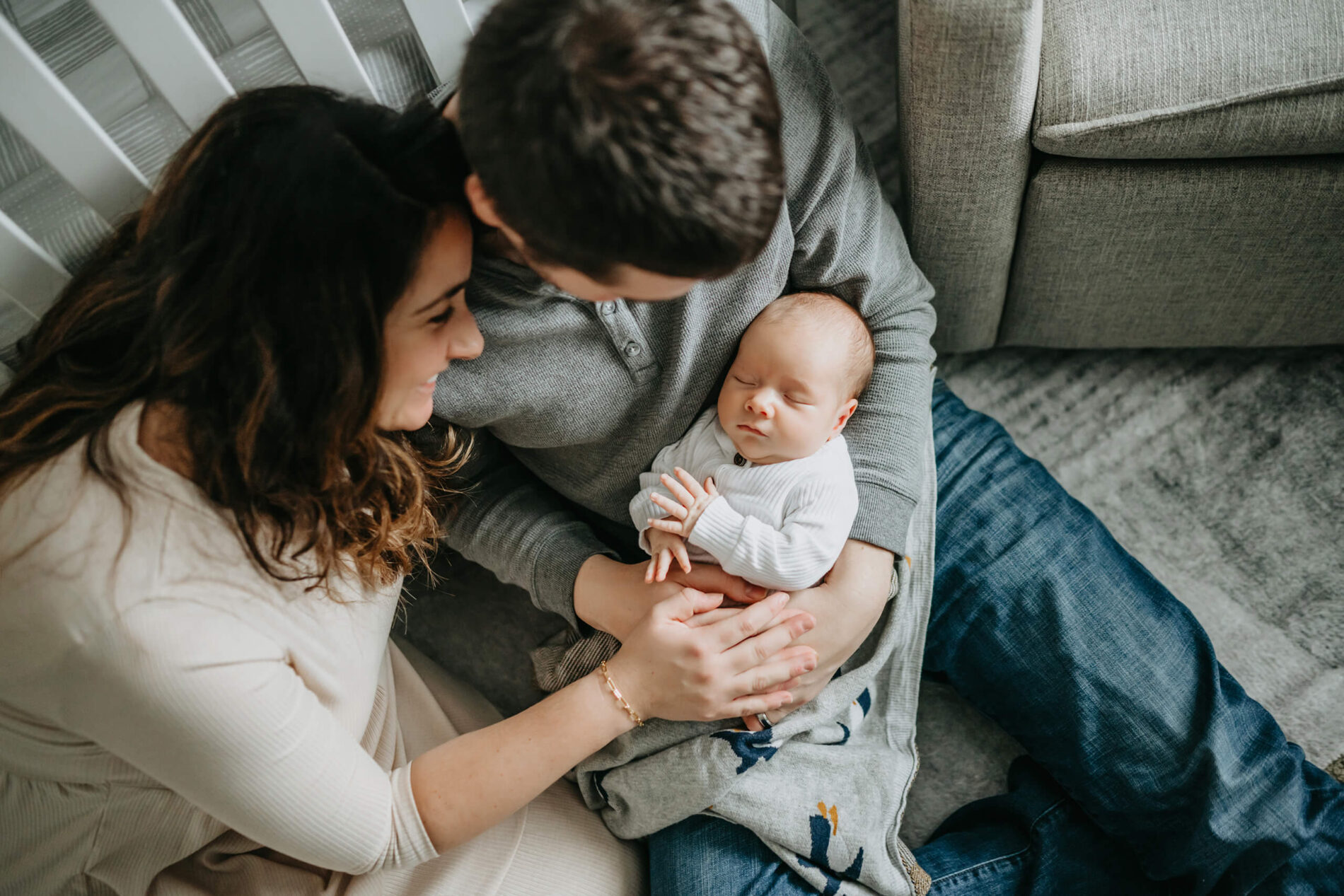 Dad cuddling on the floor of a nursery with his newborn son and wife