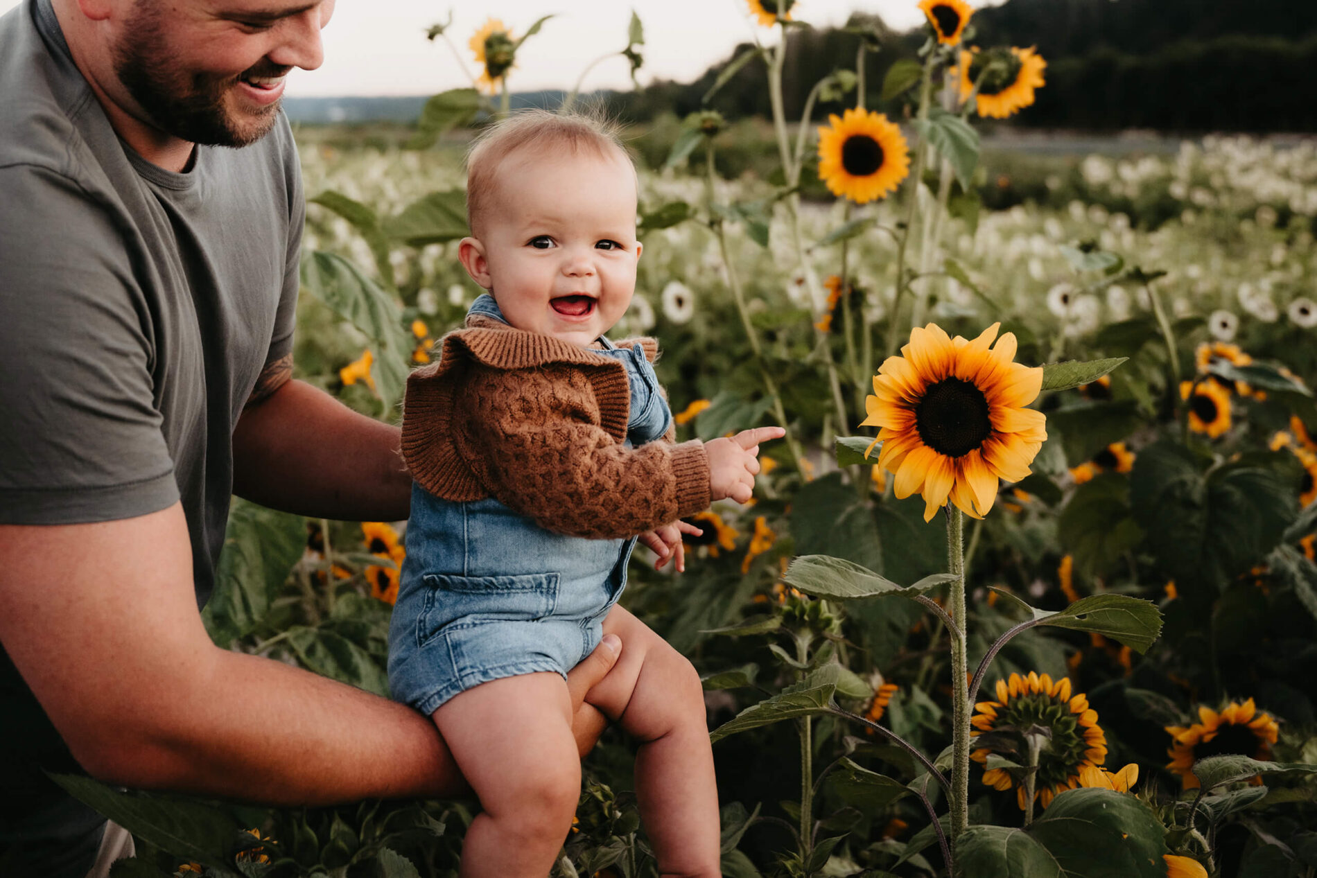 Dad holding his toddler son next to a large sunflower