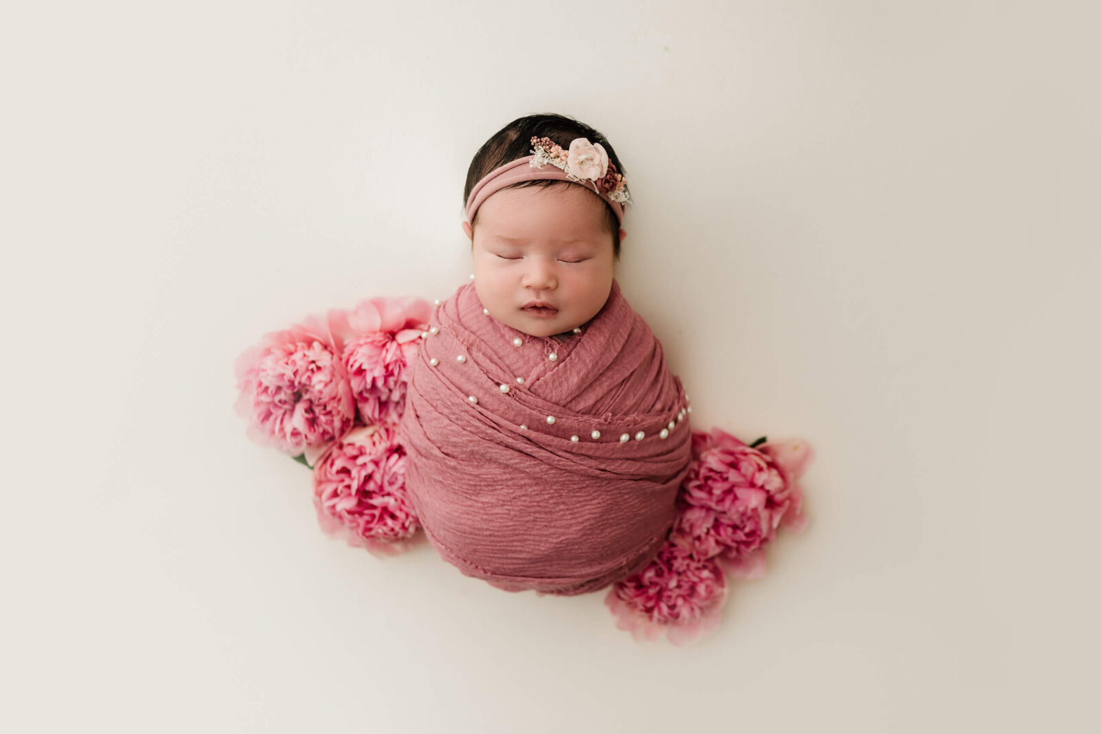 Beautifully wrapped sleeping newborn girl with flowers surrounding her