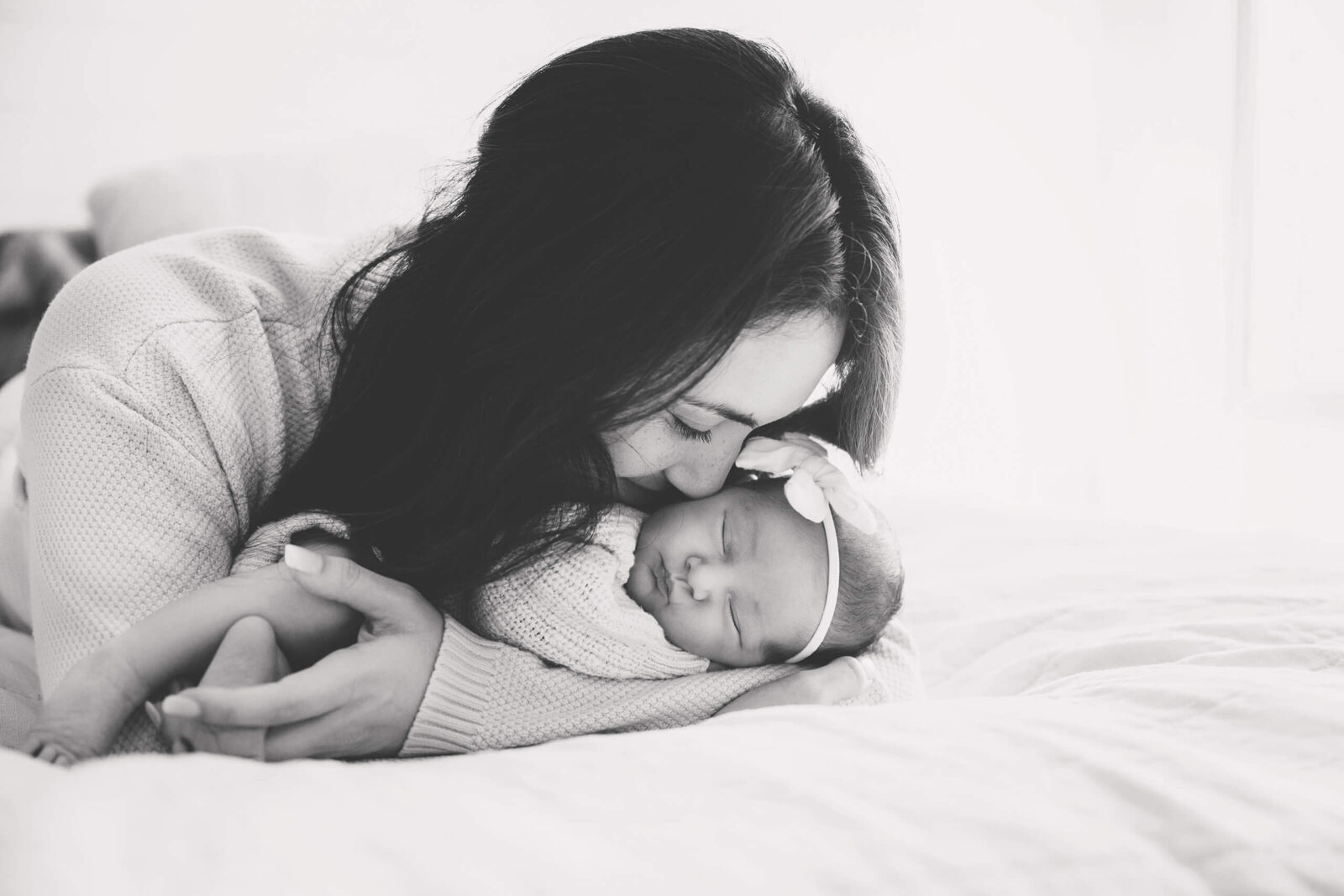 Mom snuggling with her newborn daughter on her bed