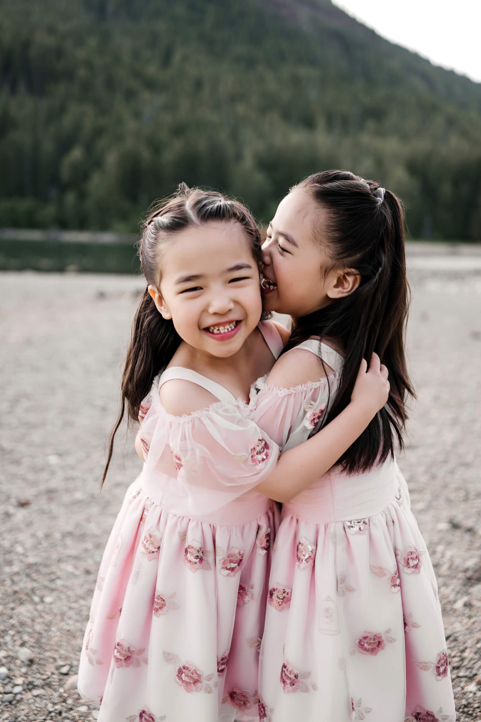 Twin girls in beautiful pink dresses hugging with mountains in the background