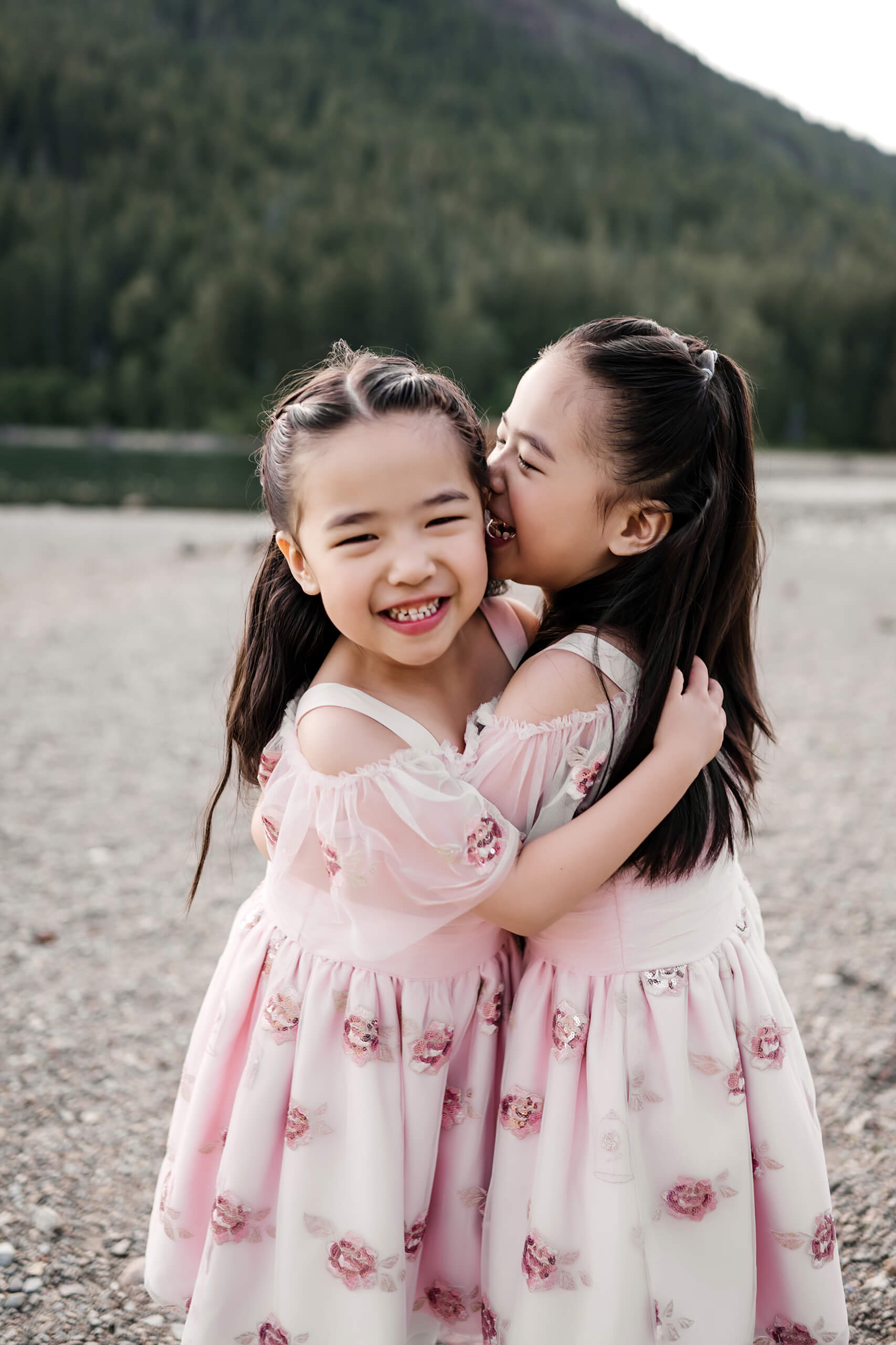 Twin girls in beautiful pink dresses hugging with mountains in the background