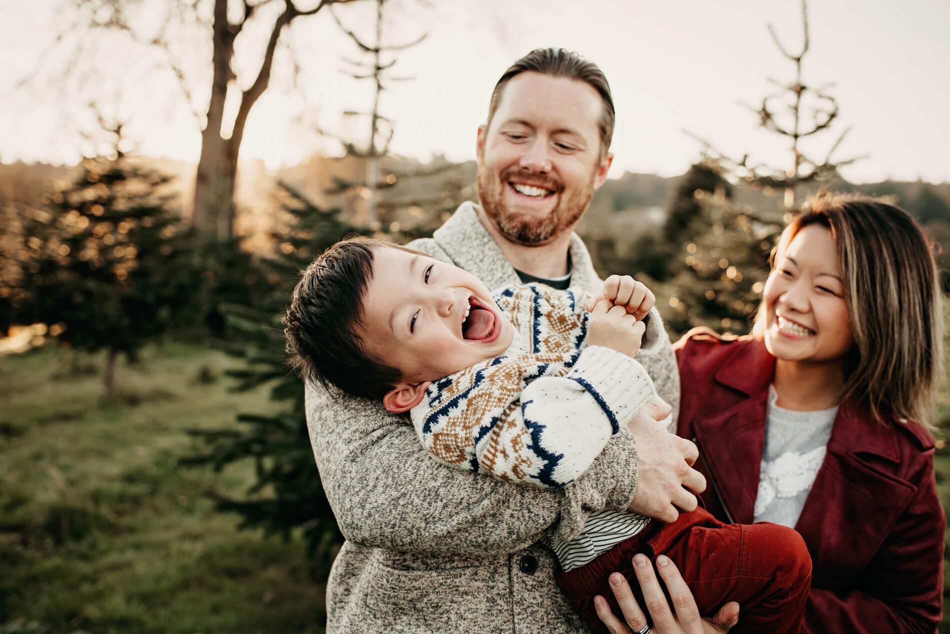 Dad tickling his son with mom smiling nearby and Christmas tree in the background