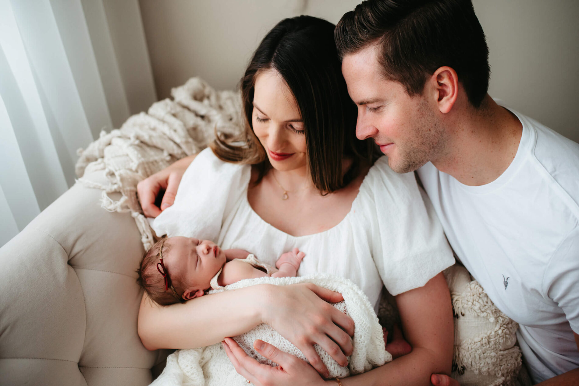 Young woman, holding her newborn daughter in her arms, with her husband lovingly looking at their daughter