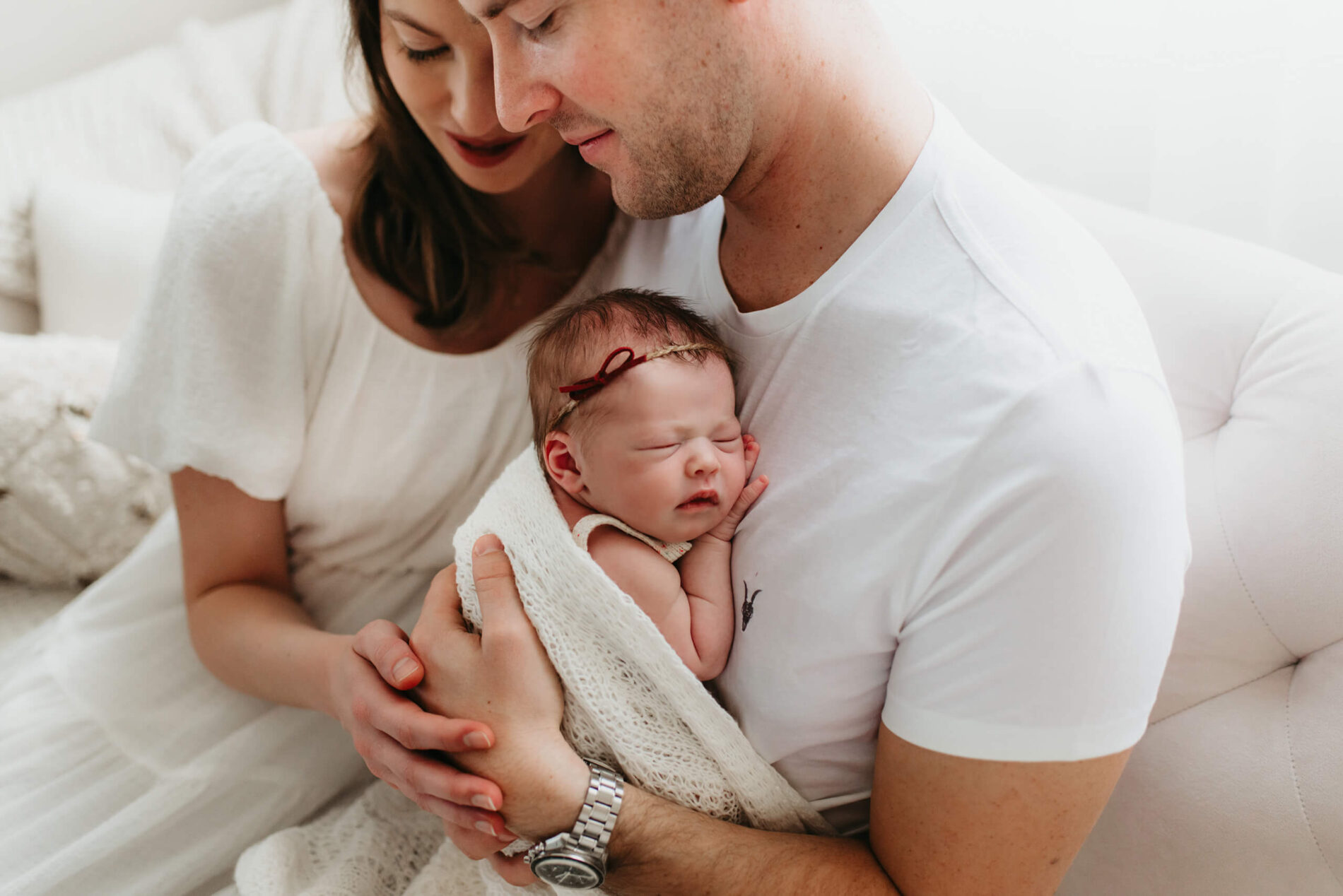 A man cradling his newborn daughter, with his wife sitting next to him