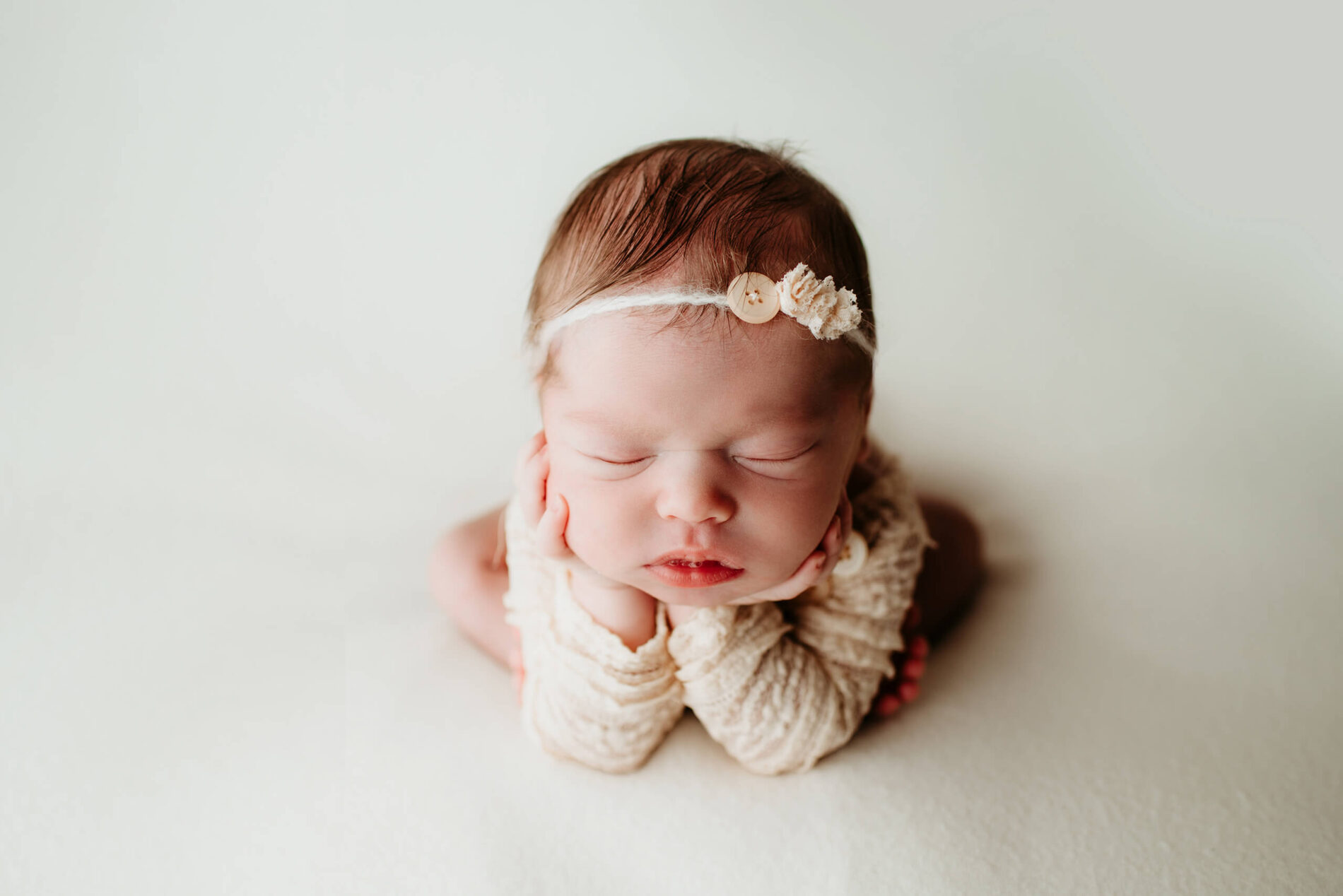 A sleeping newborn girl photographed in a "froggy" pose