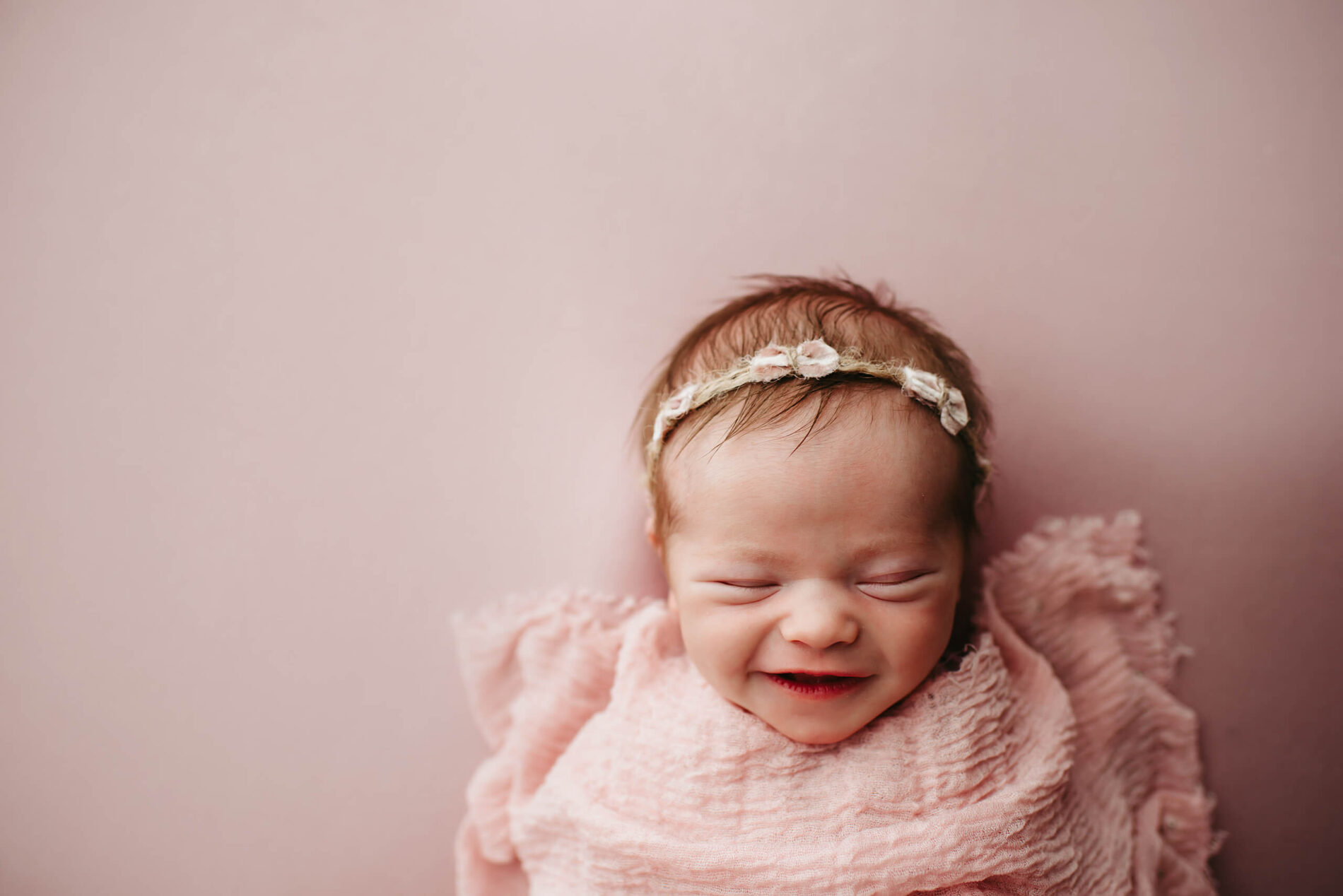A sleeping newborn girl wrapped in pink blankets, smiling