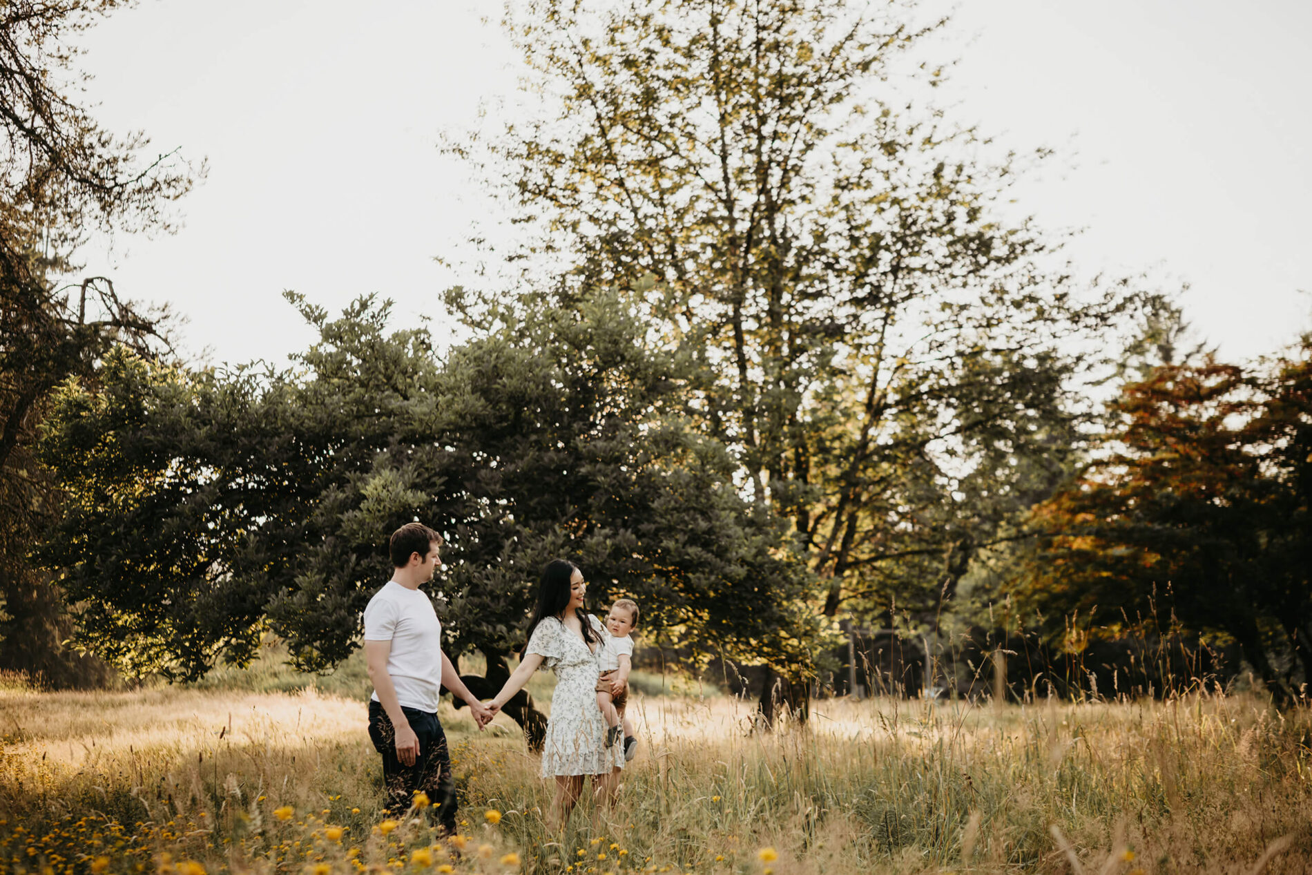 Family of three walking through a field in a park