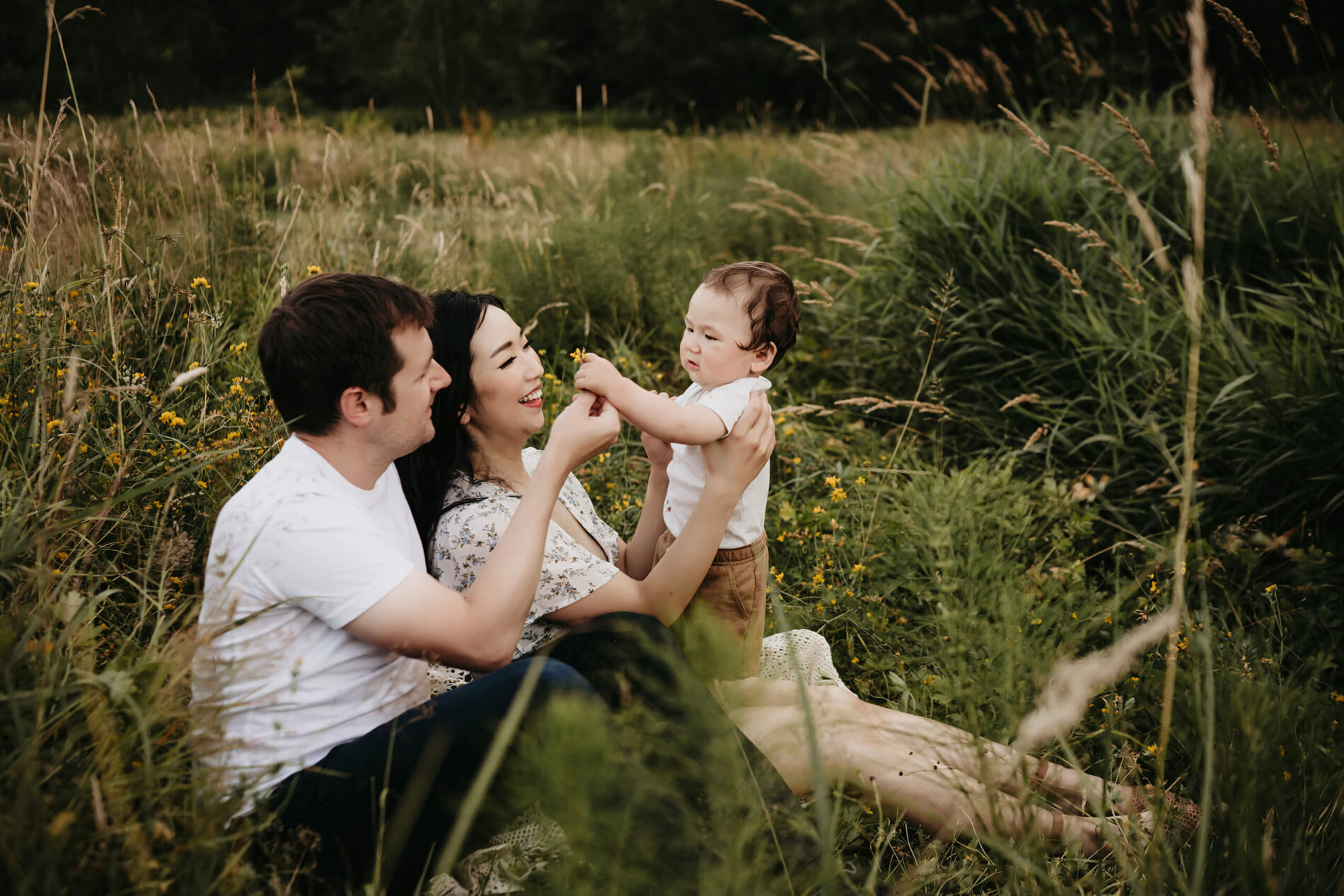 Mom and dad sitting in a meadow playing with their son