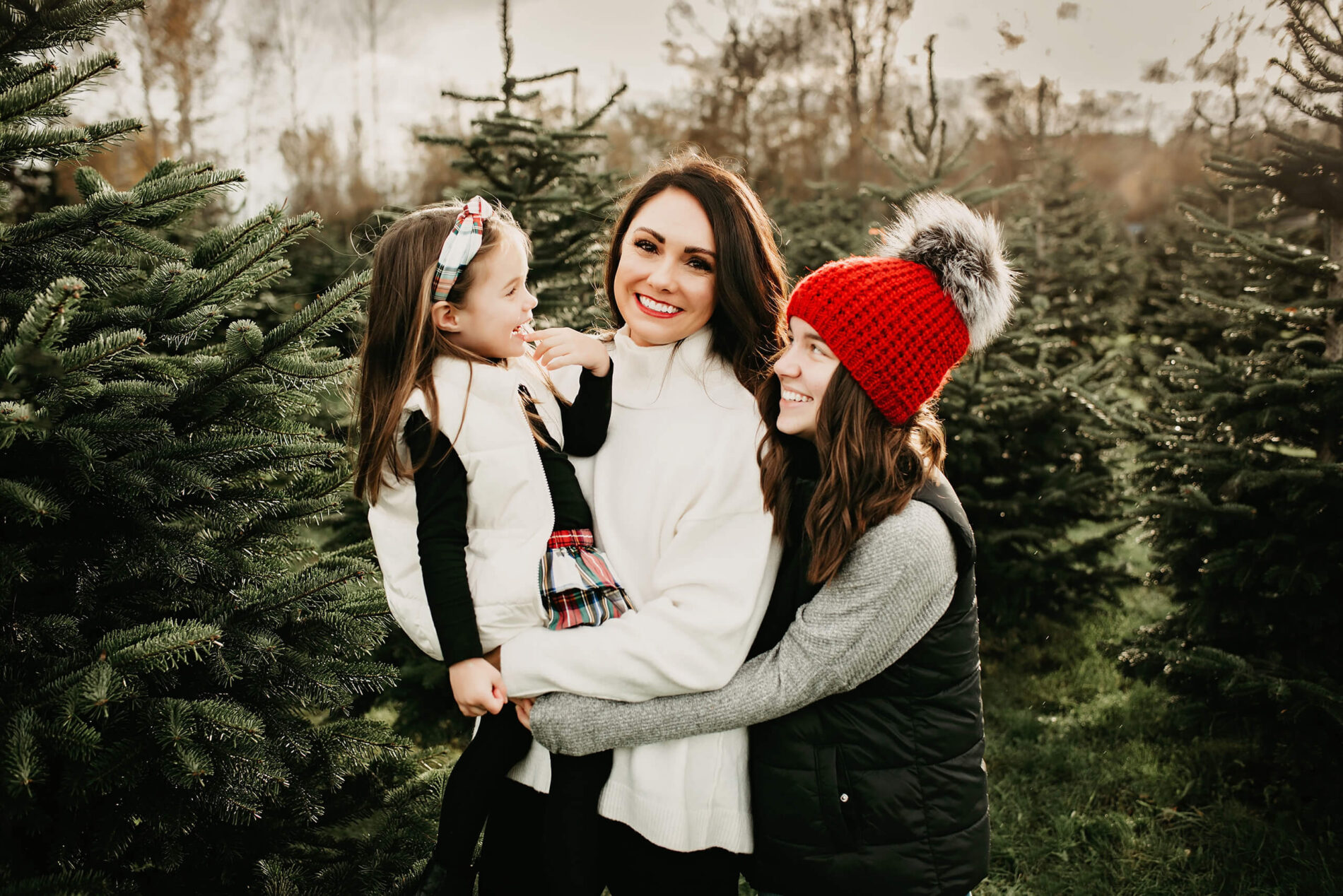 A woman posing with her two daughters for a holiday photo at a Christmas tree farm