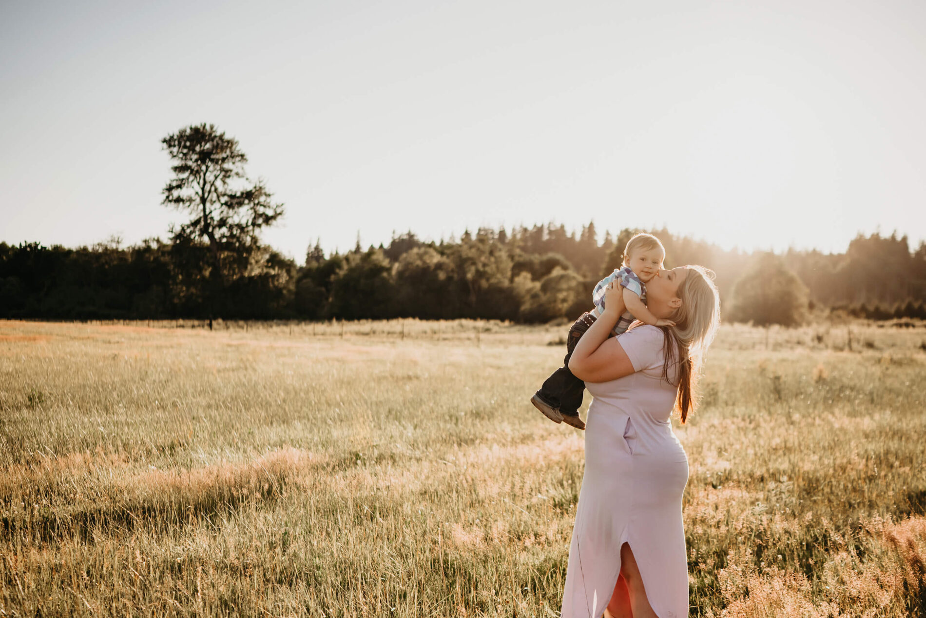 Mom holding and kissing her toddler son in a stunning field during sunset