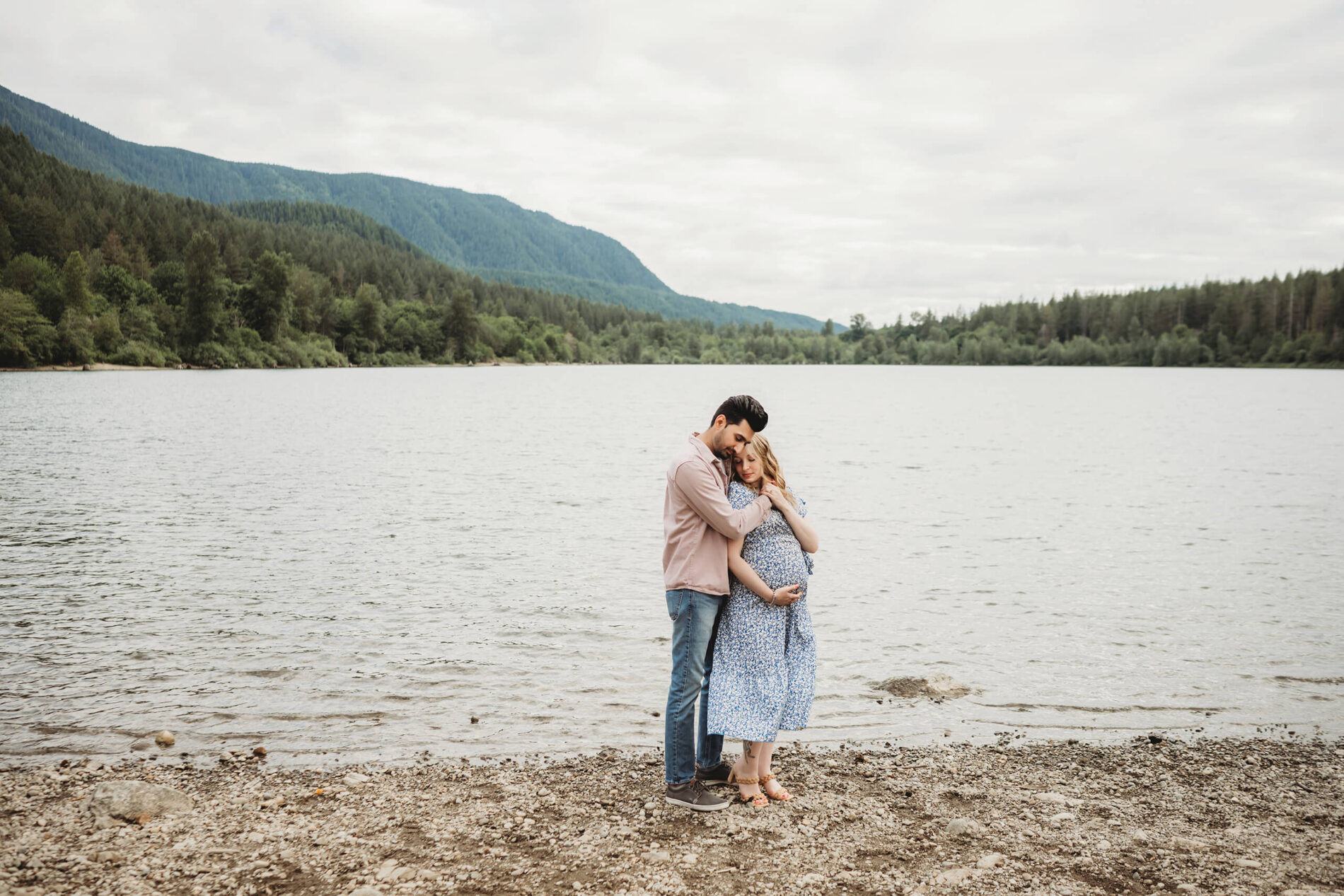 Man hugging his pregnant wife with beautiful lake and mountains in the background