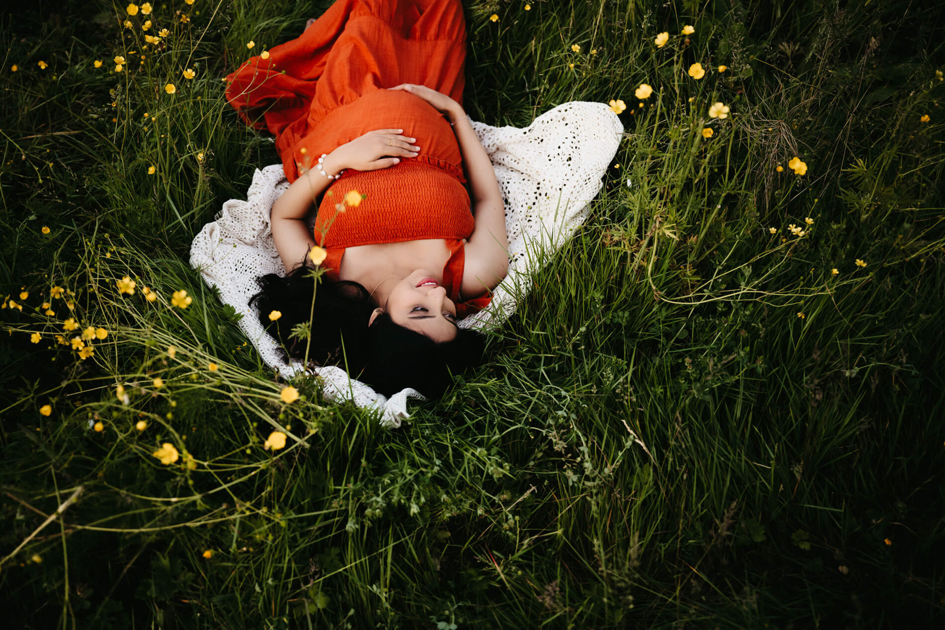 A pregnant woman in a red dress lying on the ground in a meadow
