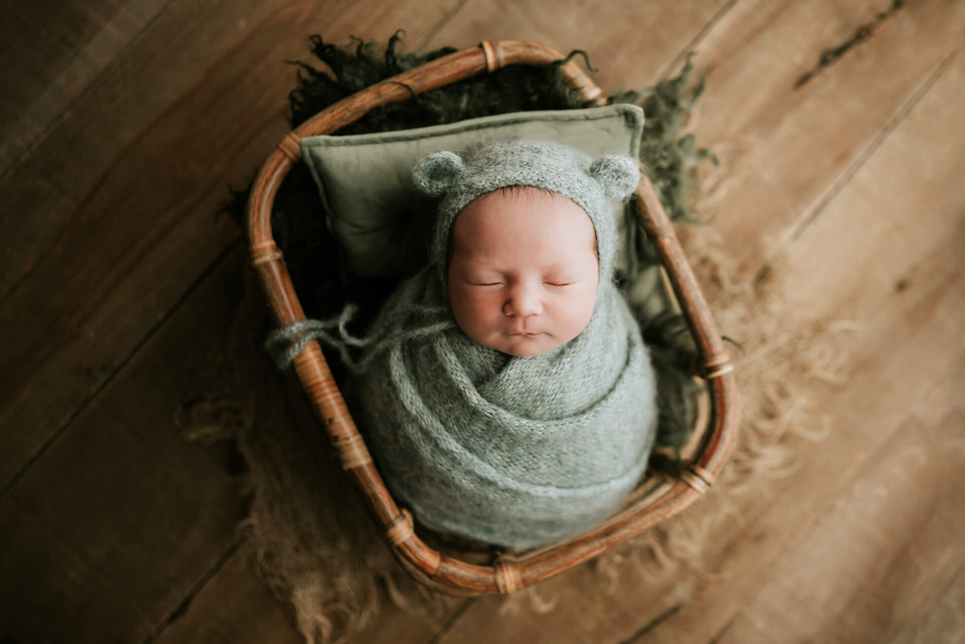 Newborn photo session: newborn boy wrapped in green blanket, sleeping in a basket