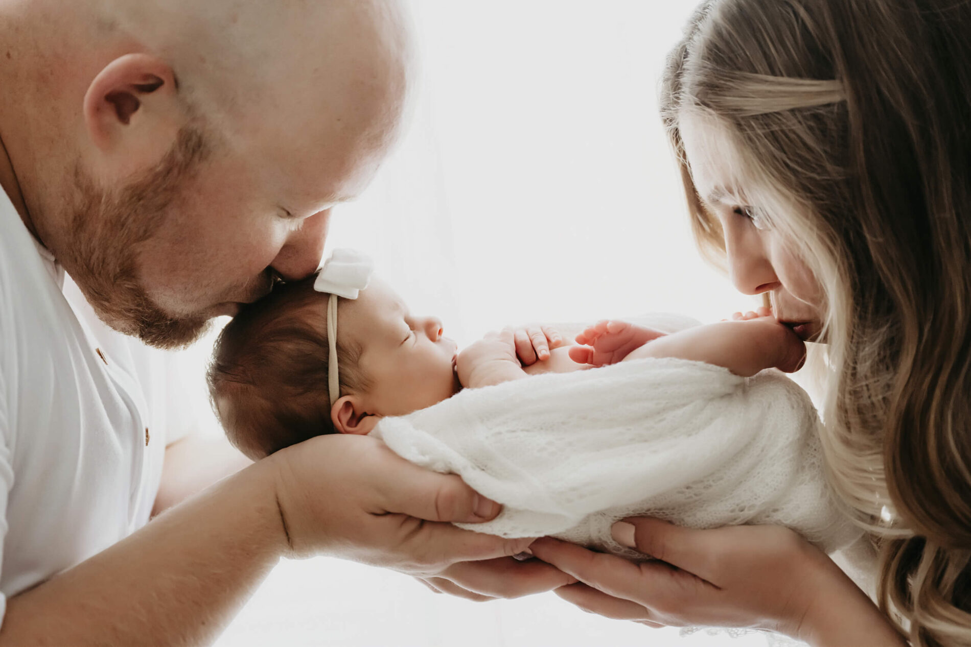 Newborn photo session of dad kissing his daughter's head and mom kissing her daughter's foot
