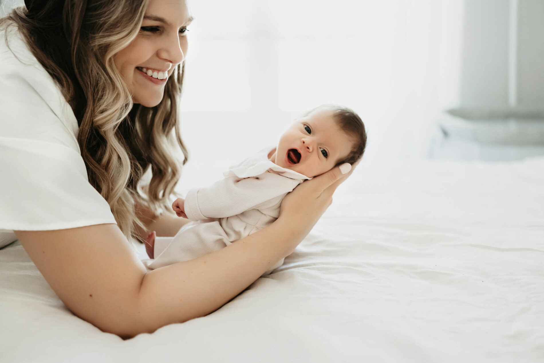 In-home newborn photo of mom holding her daughter on her bed