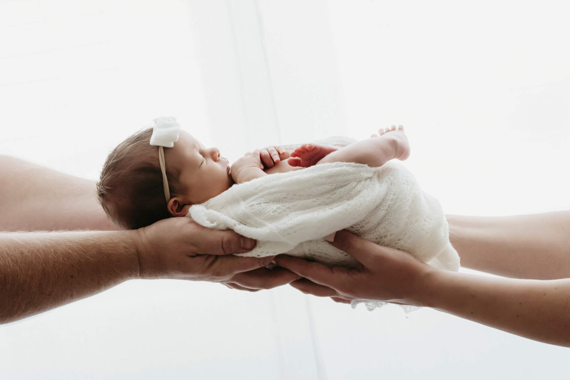 Newborn photo session of mom and dad holding their newborn daughter by a window