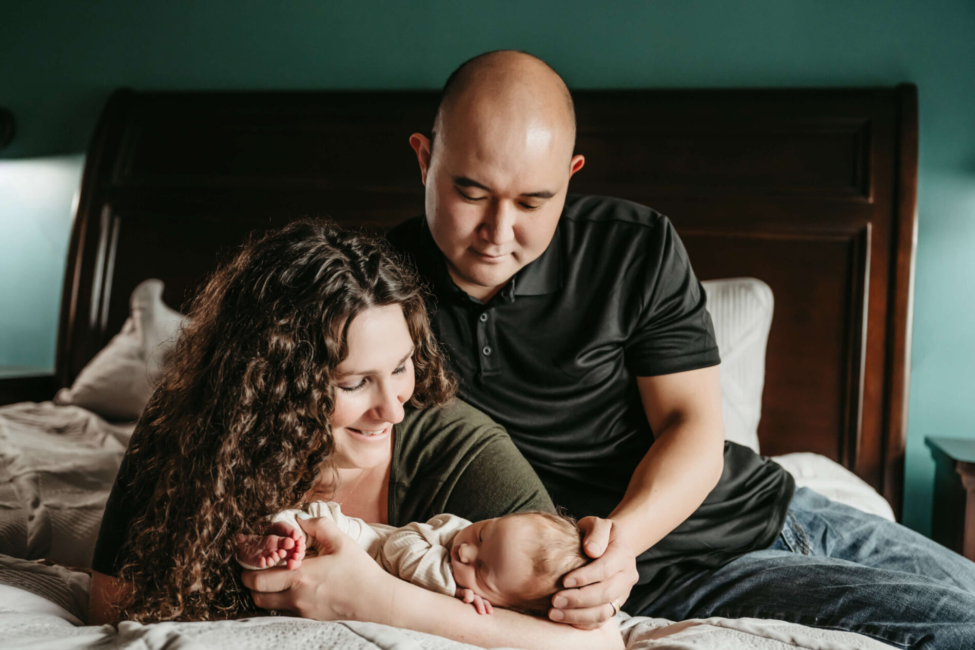 In-home lifestyle newborn photo shoot: focus on parents cuddling with their newborn boy on the bed