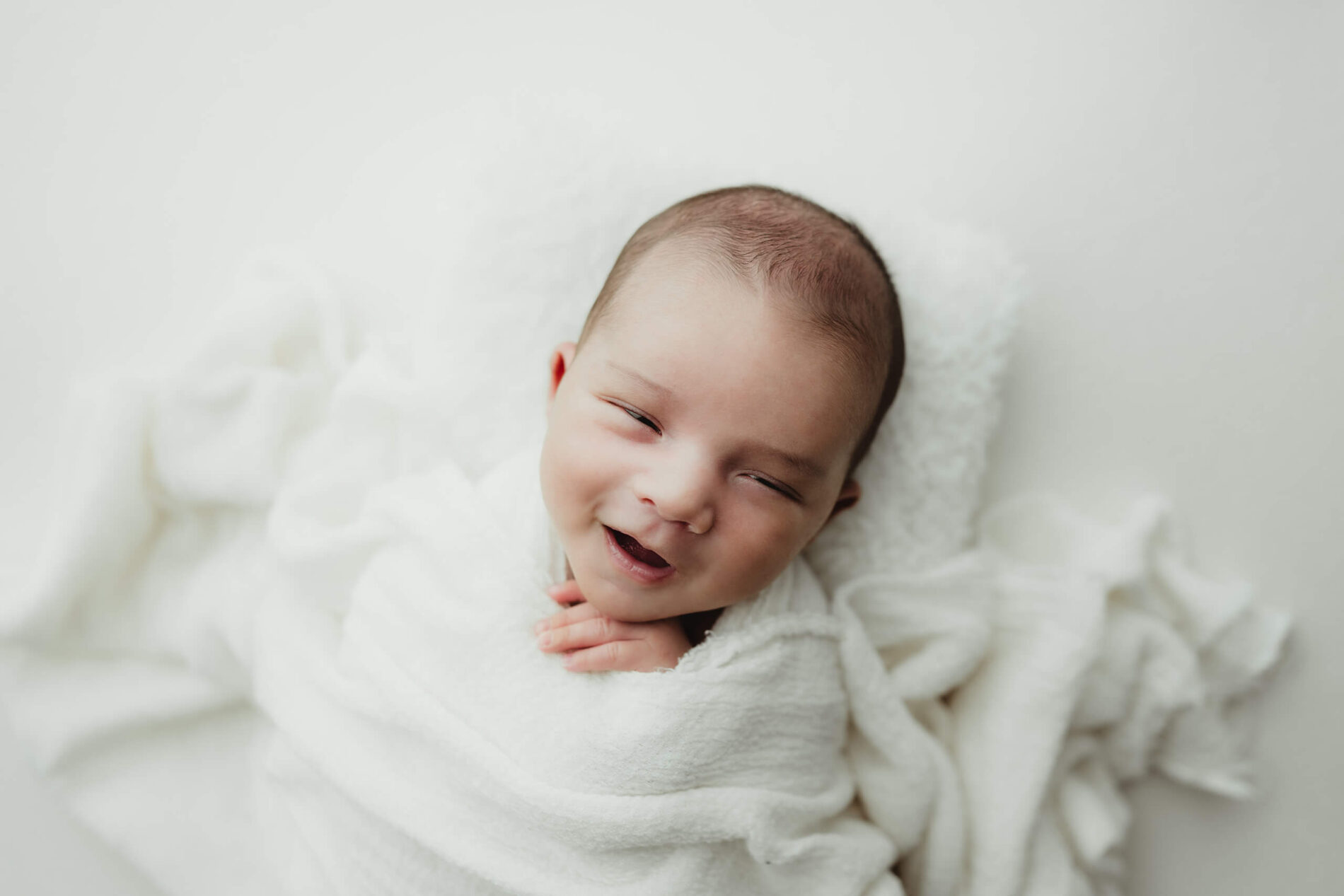 Newborn photography session: cozily-wrapped sleeping and smiling newborn boy