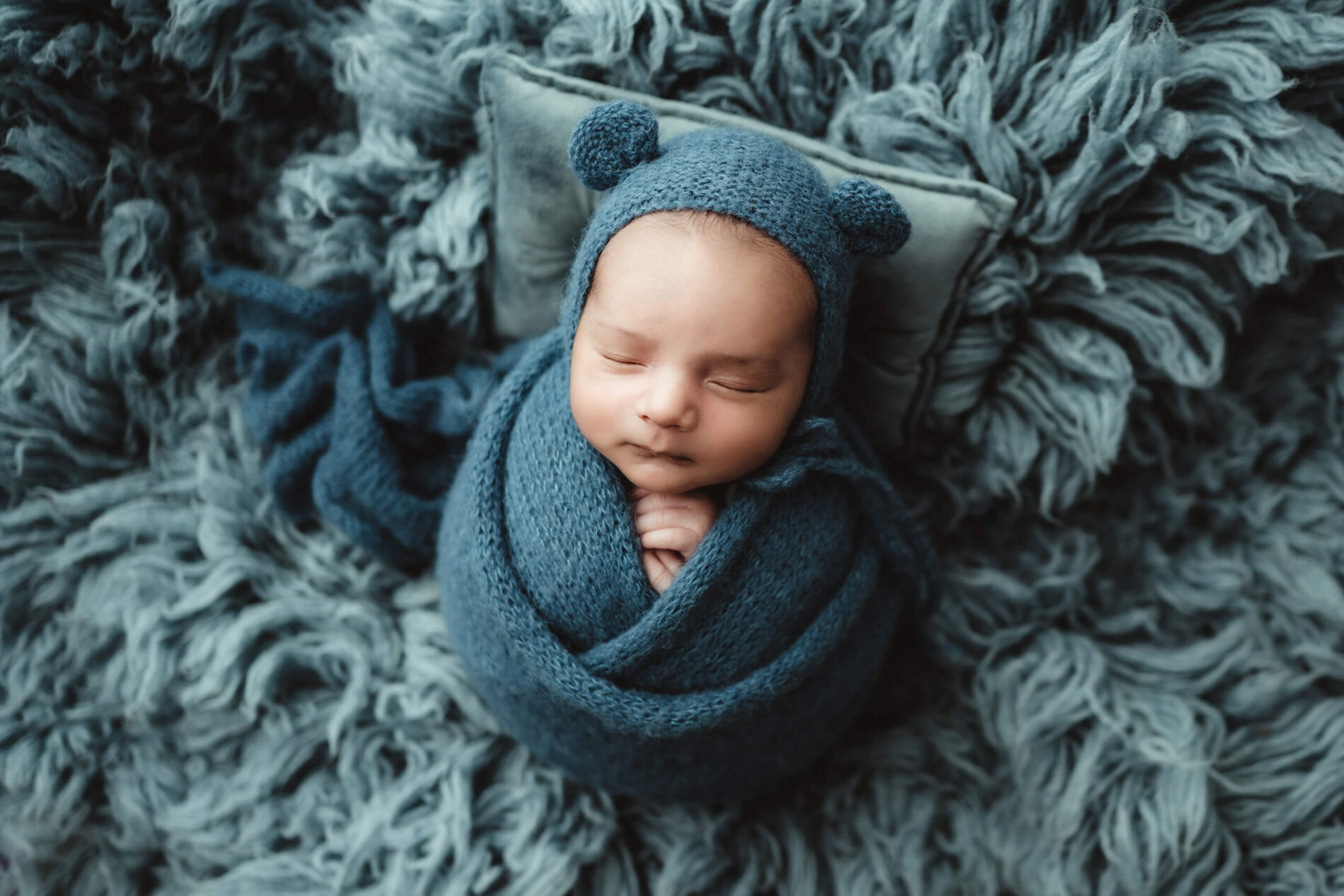 Newborn photography session: cozily-wrapped sleeping newborn boy in a cute hat