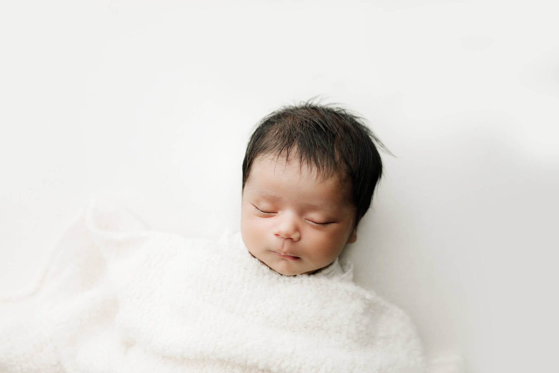 Unique newborn photography of a boy sleeping peacefully under a white blanket