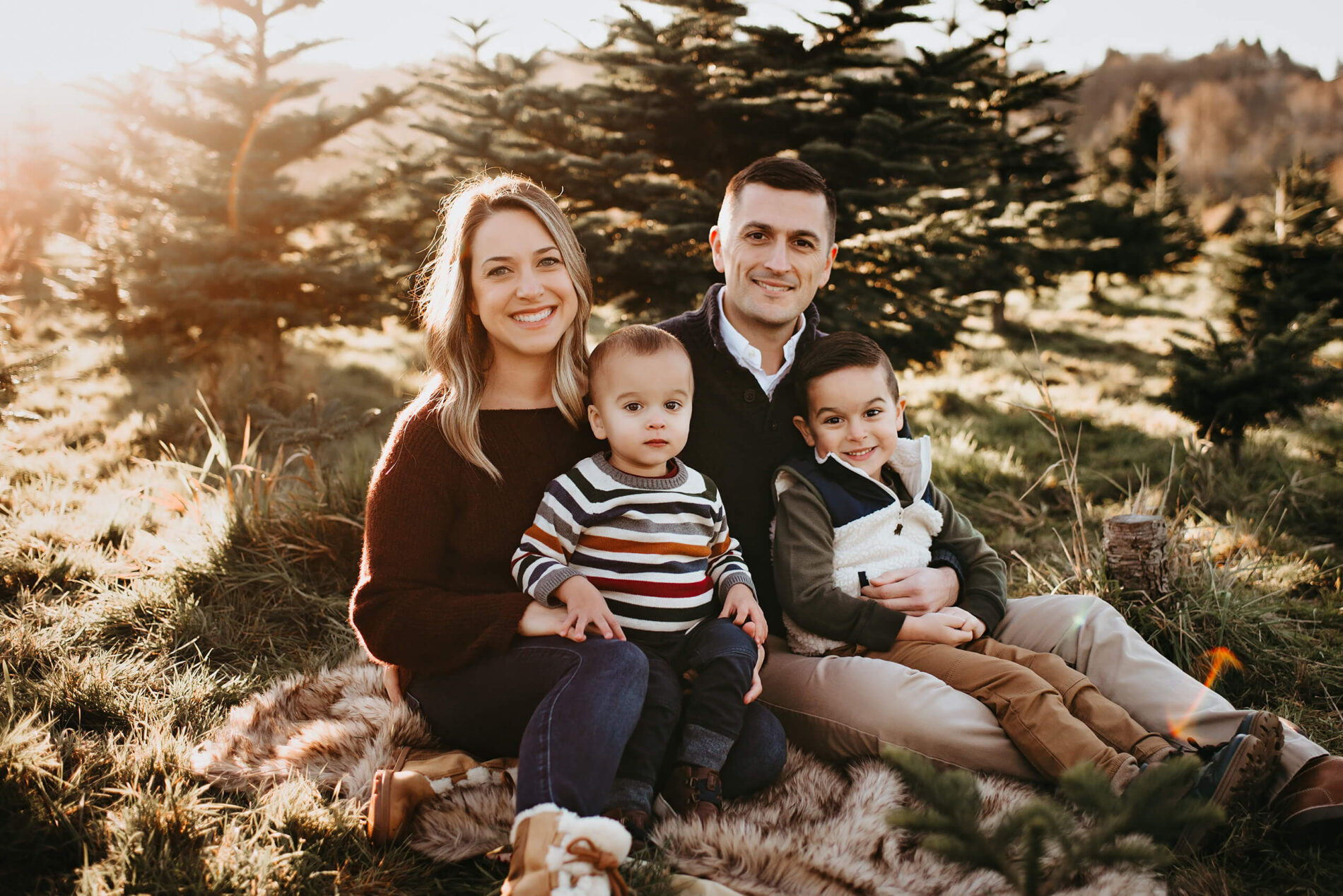 Holiday family portrait of mom, dad, and two sons at a Christmas tree farm