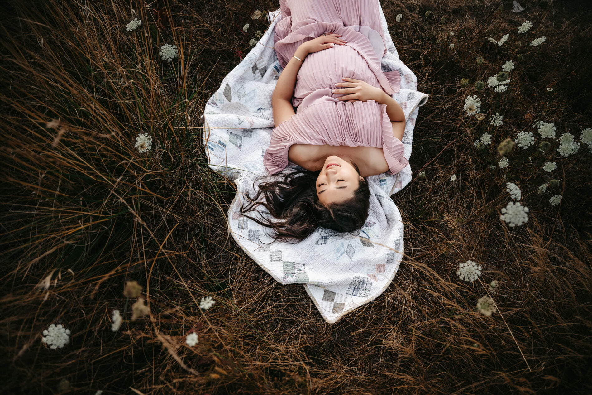 A maternity photo shoot of a young pregnant woman lying in field of wild flowers