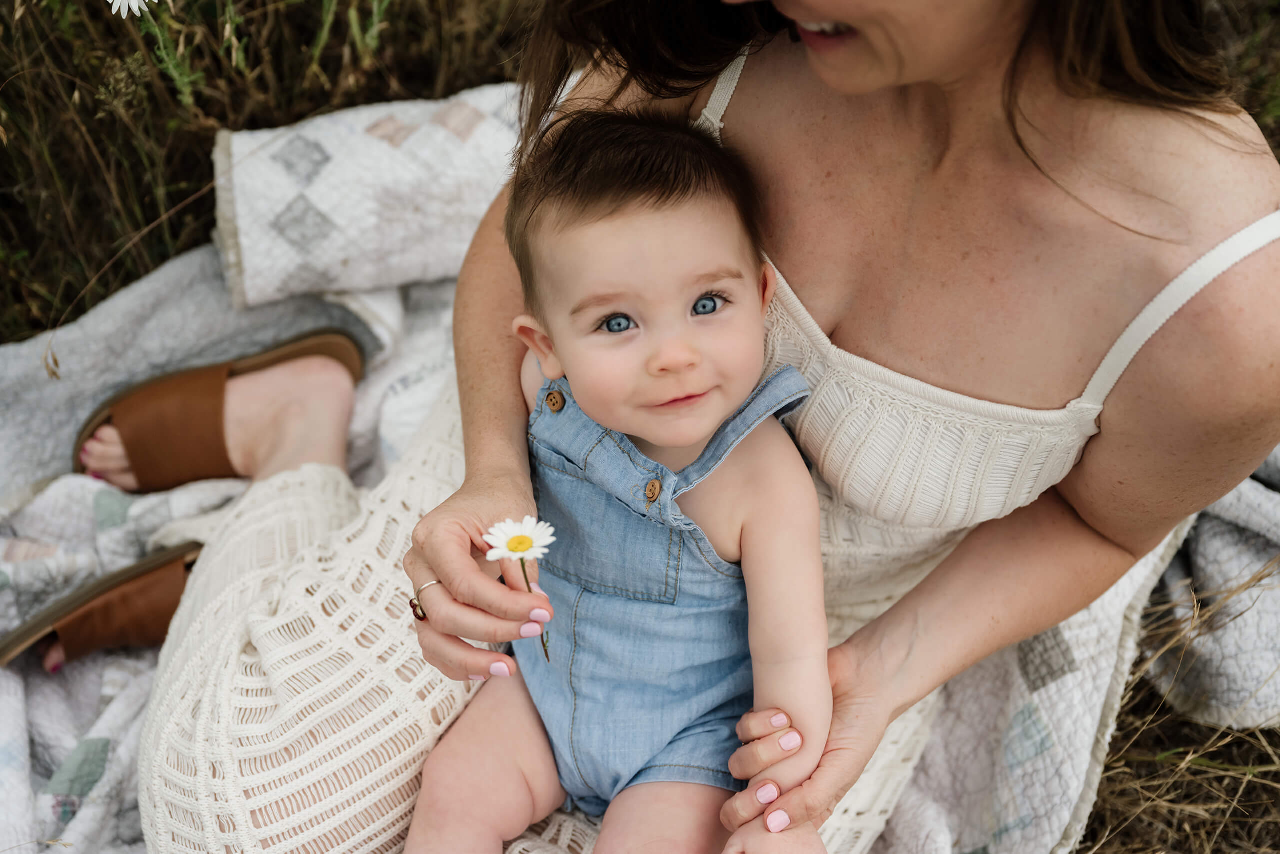 Mom holding a daisy with her baby sitting on her lap during an outdoor family session