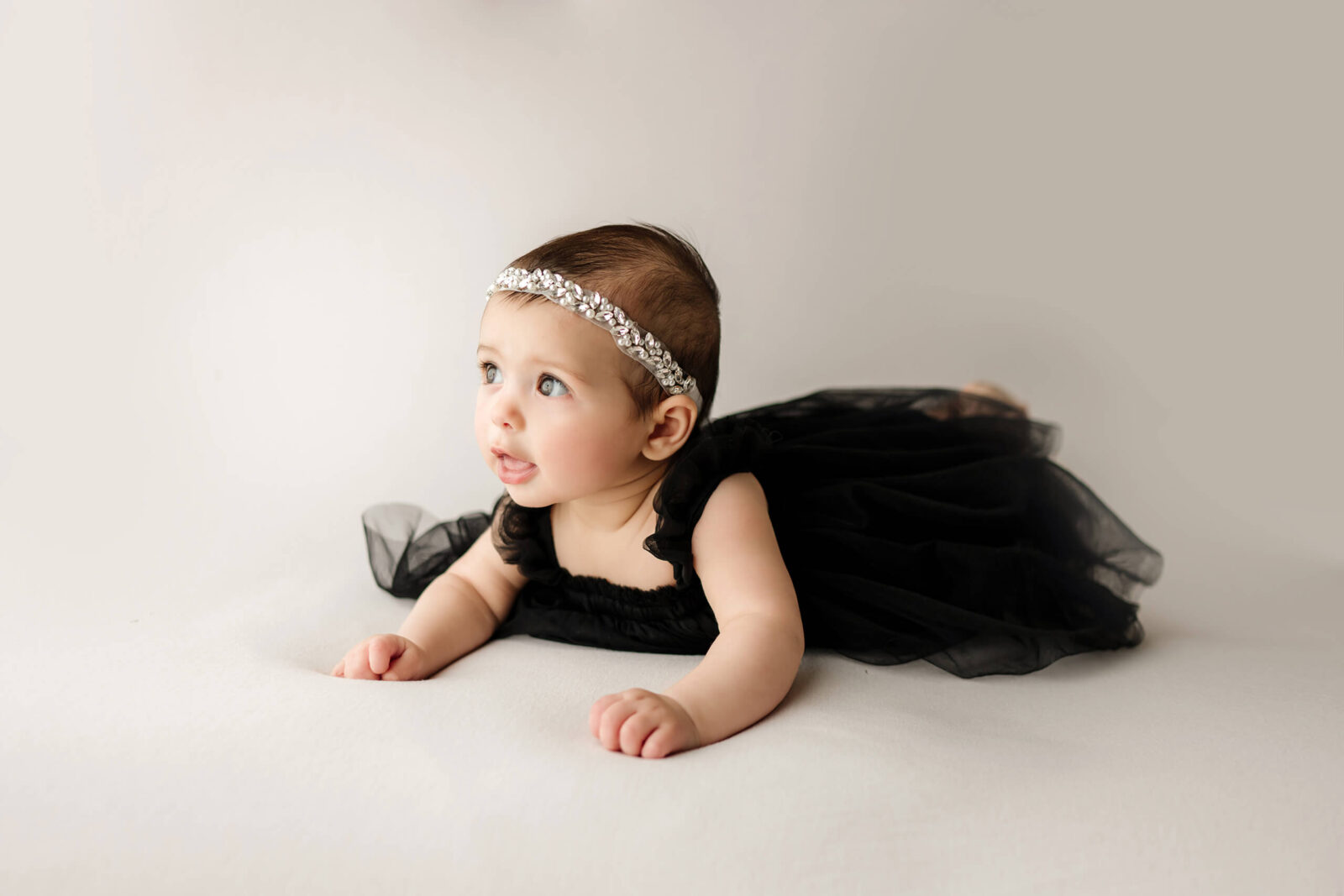 Baby in a black dress lying on her tummy during a simple studio milestone session