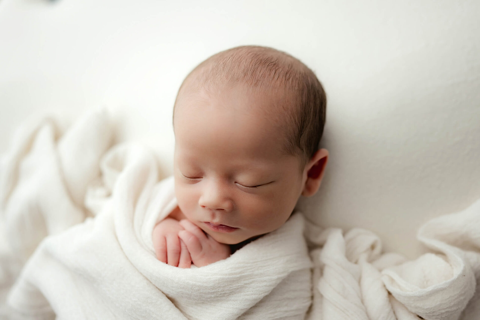Studio newborn photography session with a sleeping baby boy under white wraps