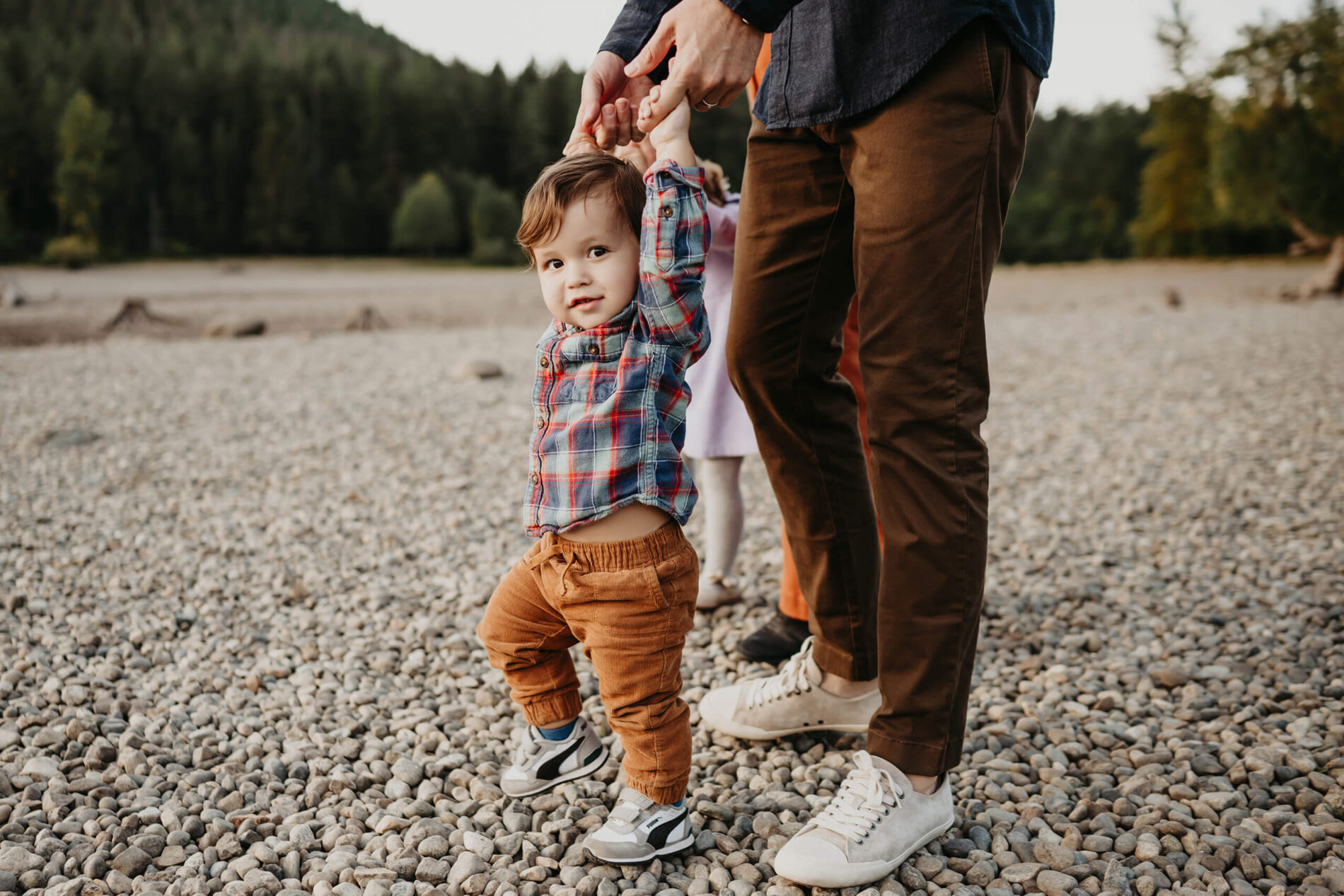 Family photo session with dad helping his toddler son walk on a beach